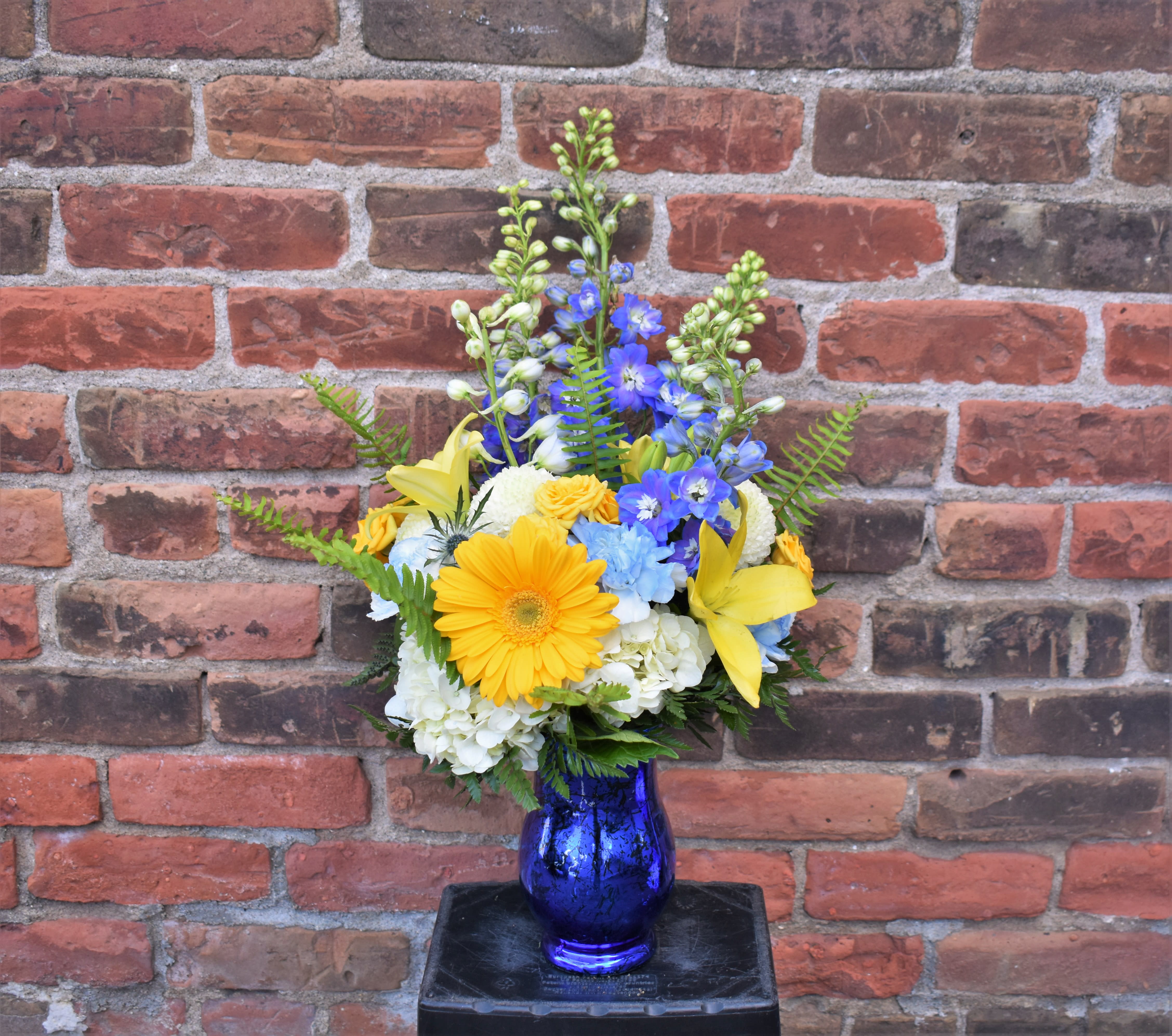 Mixed bouquet of yellow, blue, and white flowers in a blue vase