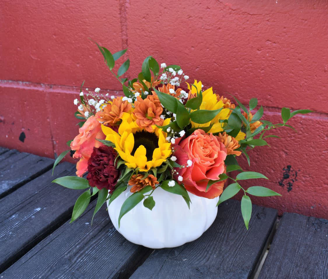Harvest Glow - Bright sunflowers, orange roses, mums and carnations are designed in a white ceramic pumpkin container and accented by greens and babysbreath...the perfect centerpiece for a Thanksgiving table, or to give as a gift! 