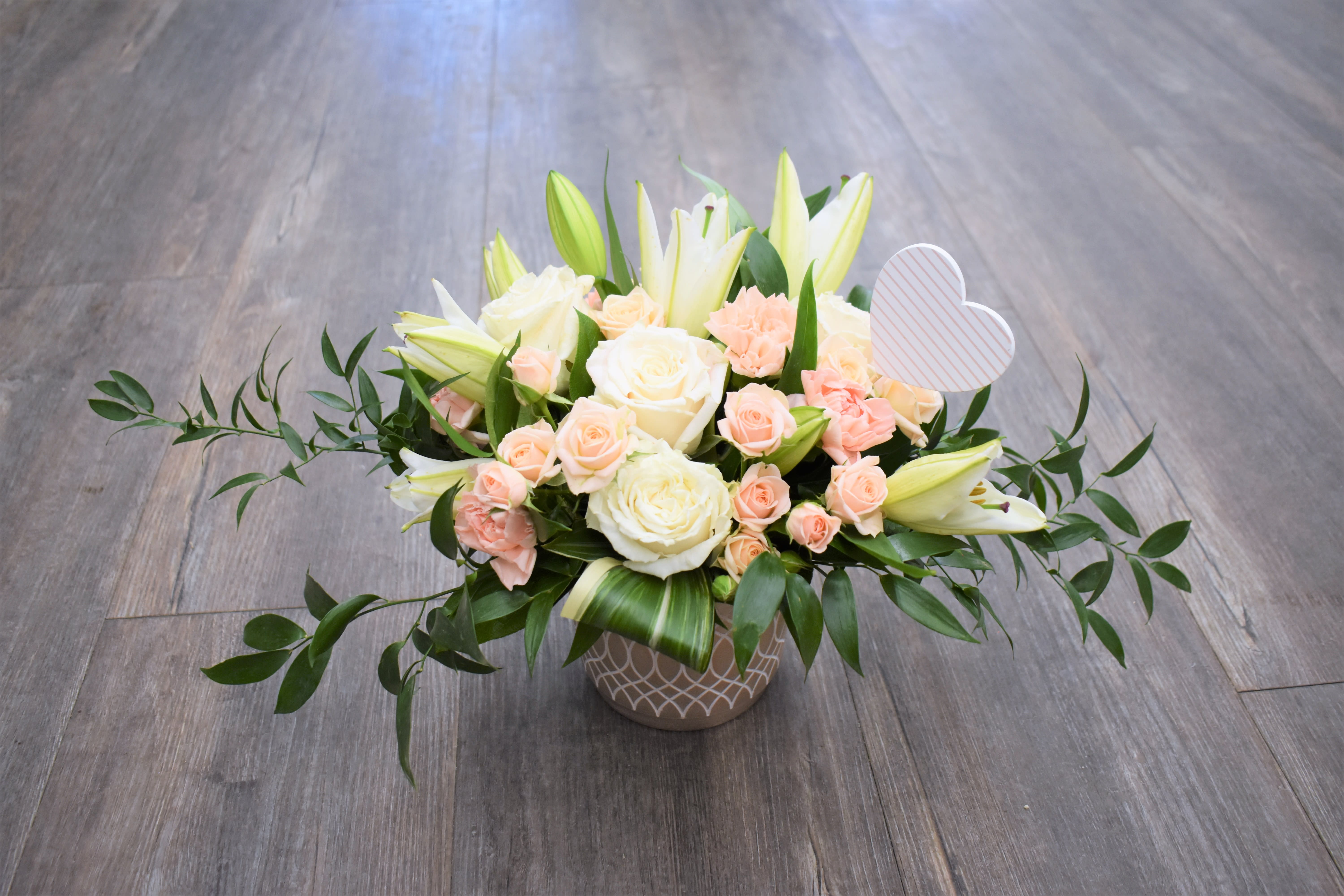 Low floral arrangement of white roses, lilies, and peach spray roses in a patterned vase