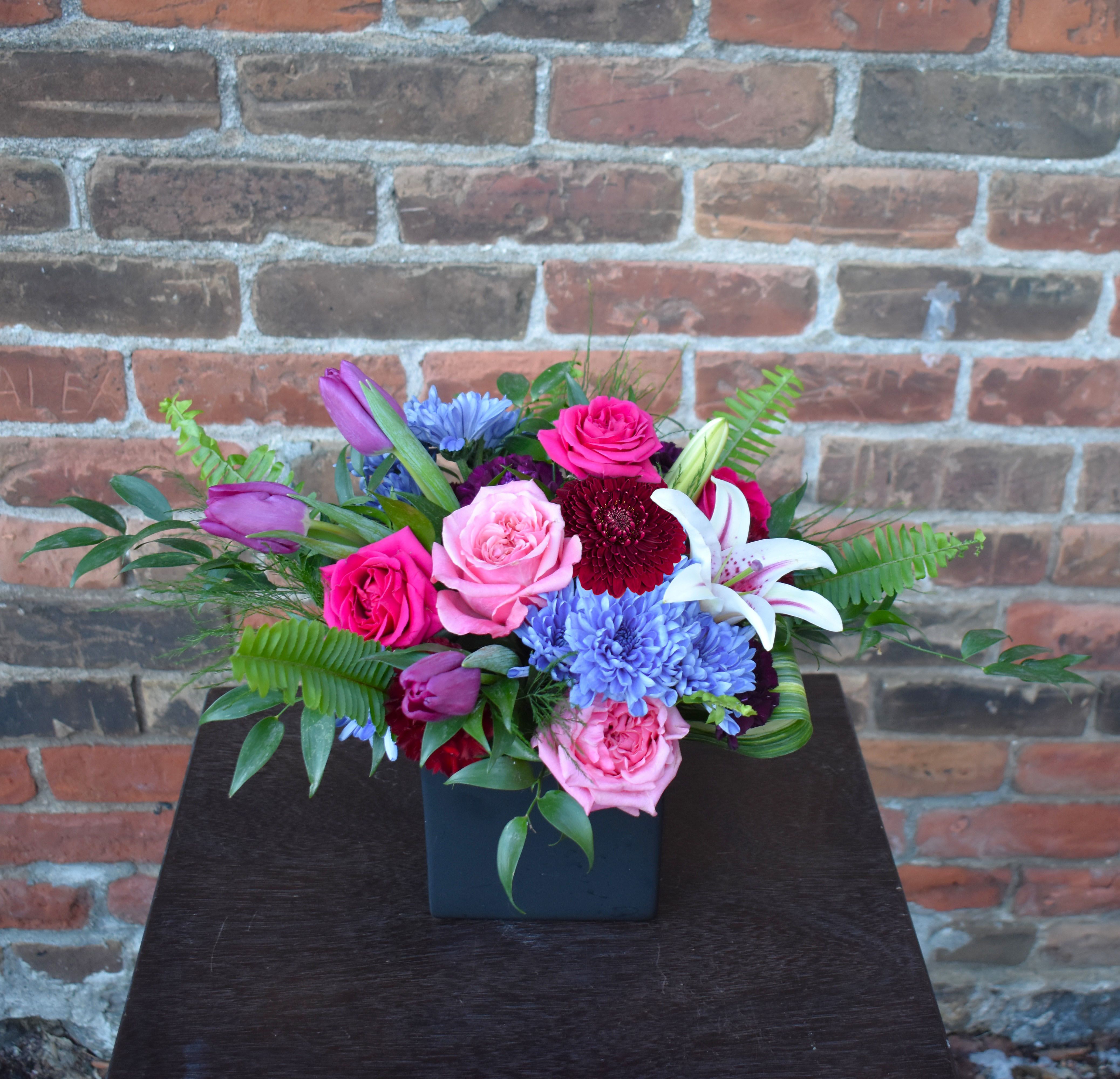Mixed bouquet in a black square vase with pink, purple, blue, and white flowers