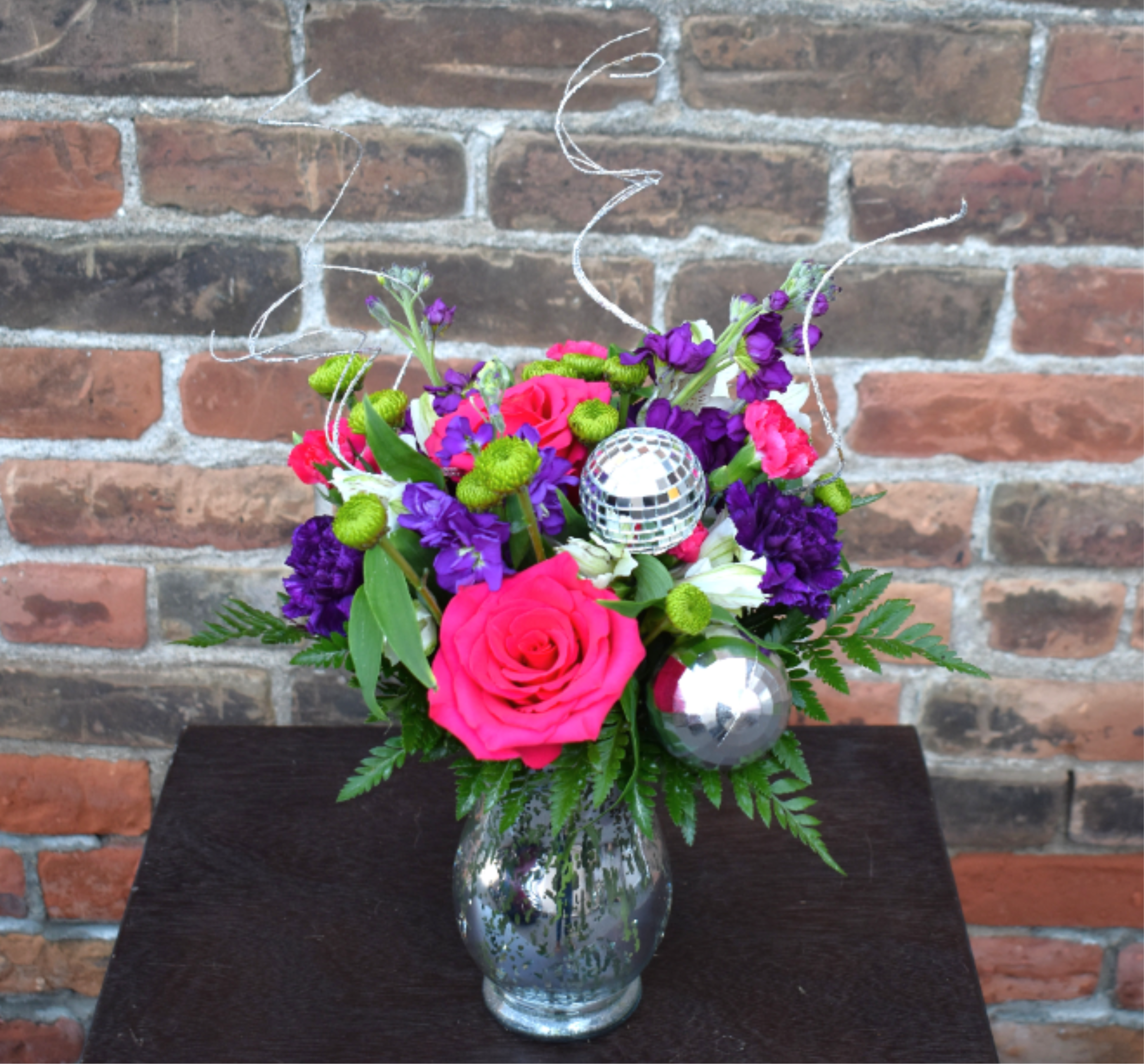 Bright pink and purple flower arrangement in a glass vase with disco balls
