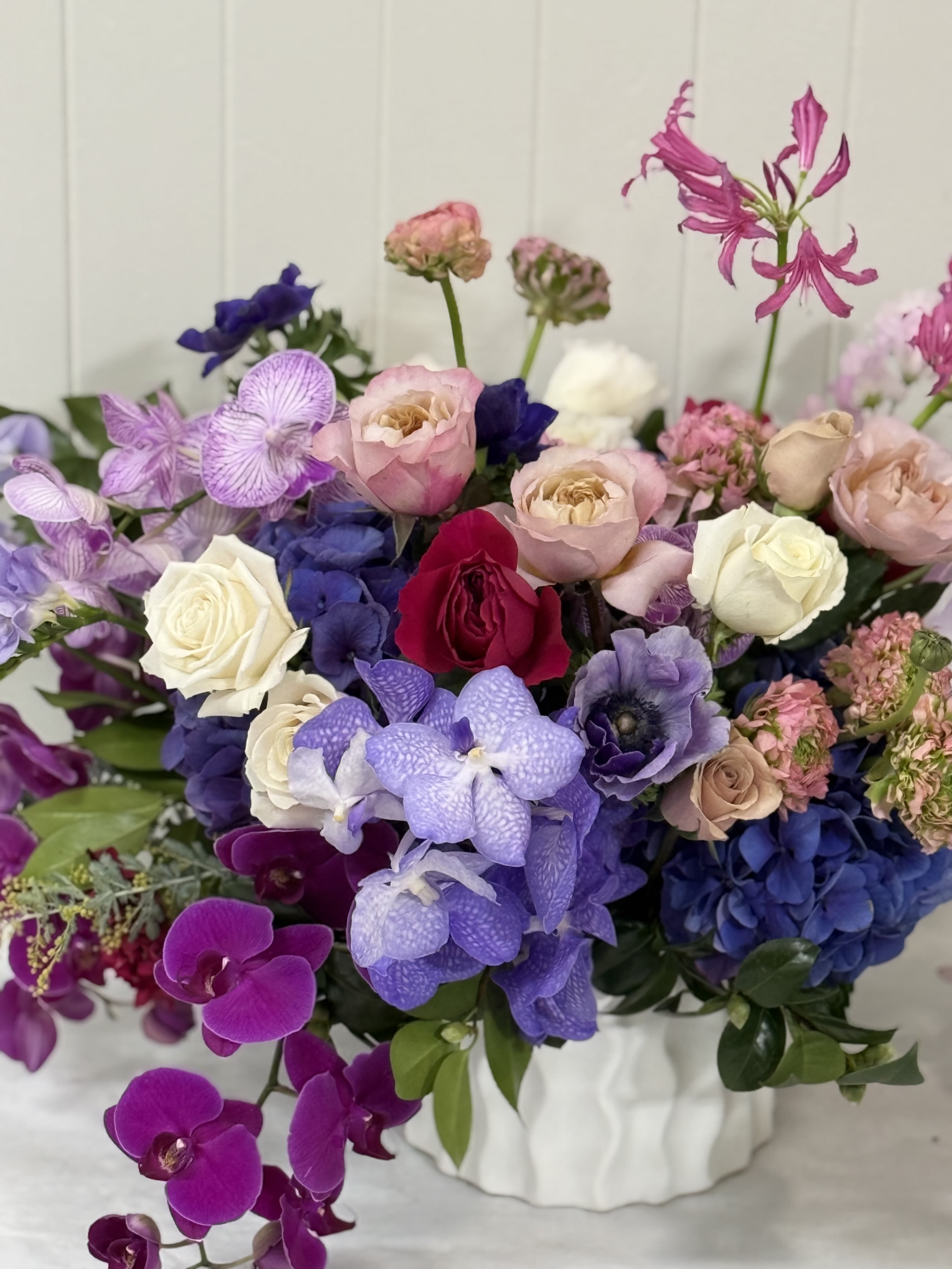 Mixed bouquet of roses, orchids, and hydrangeas in a white vase