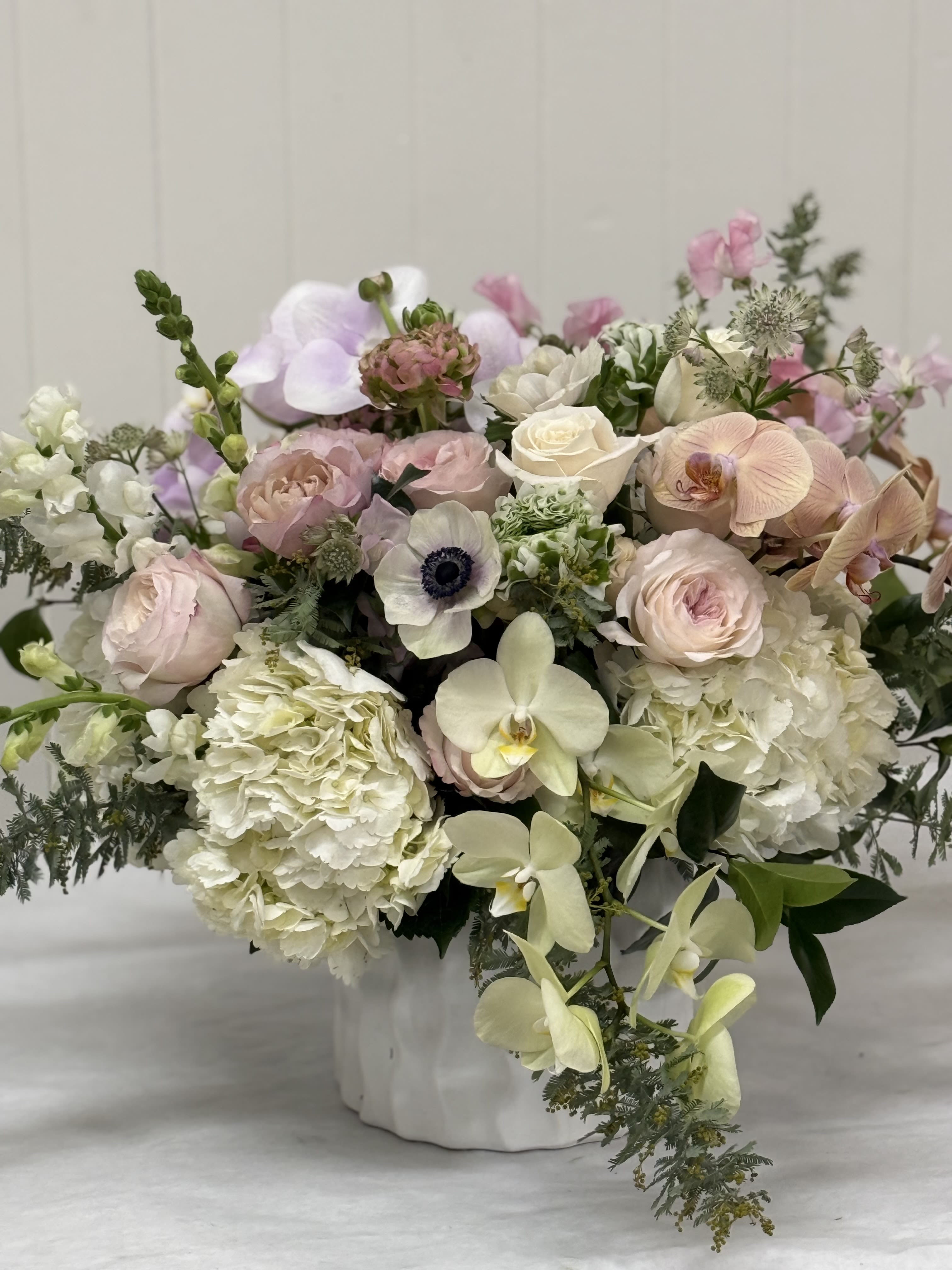 Pastel bouquet with roses, hydrangeas, orchids, and anemones in a white vase