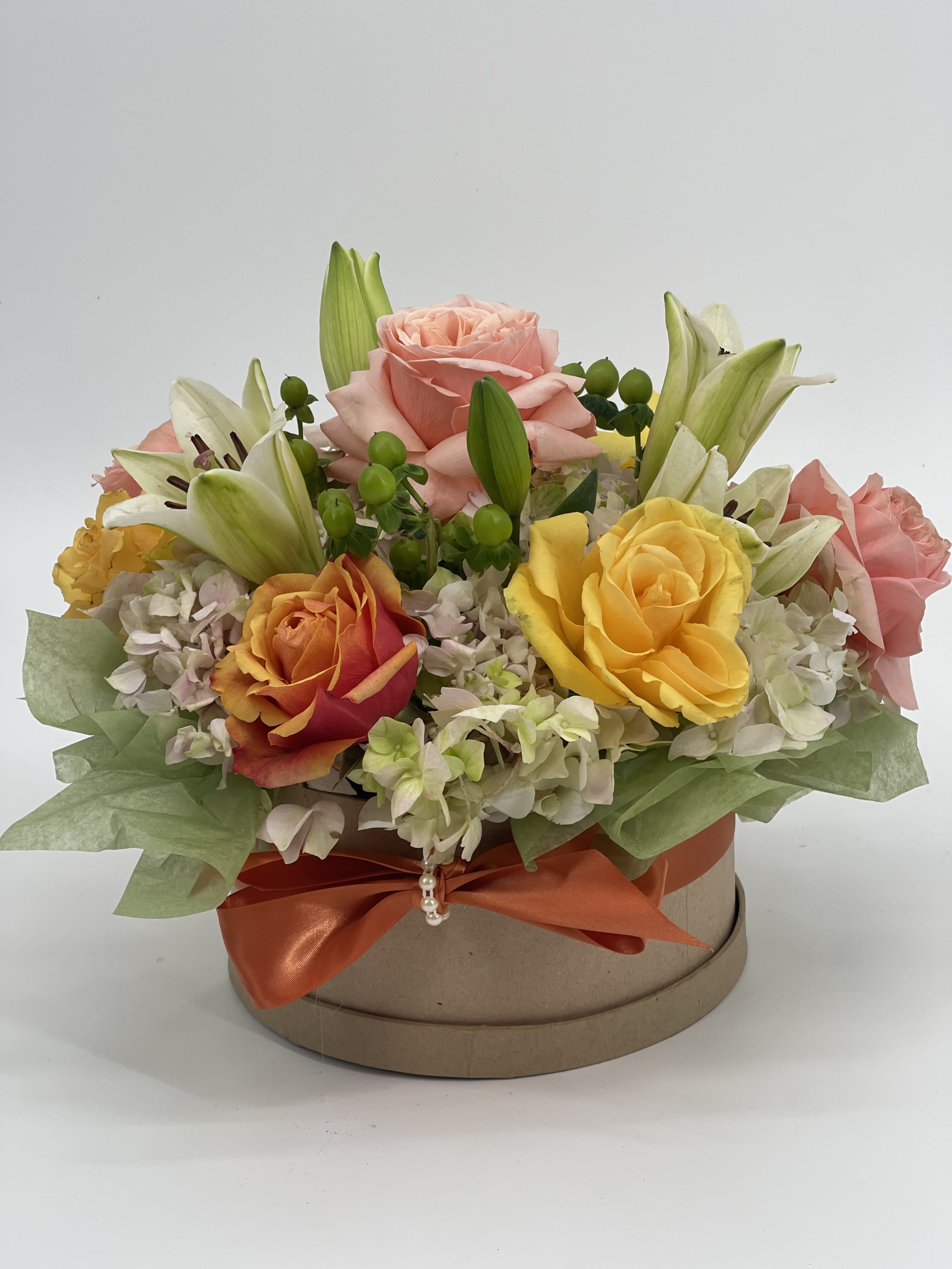 Mixed roses and lilies arranged in a round gift box with an orange ribbon