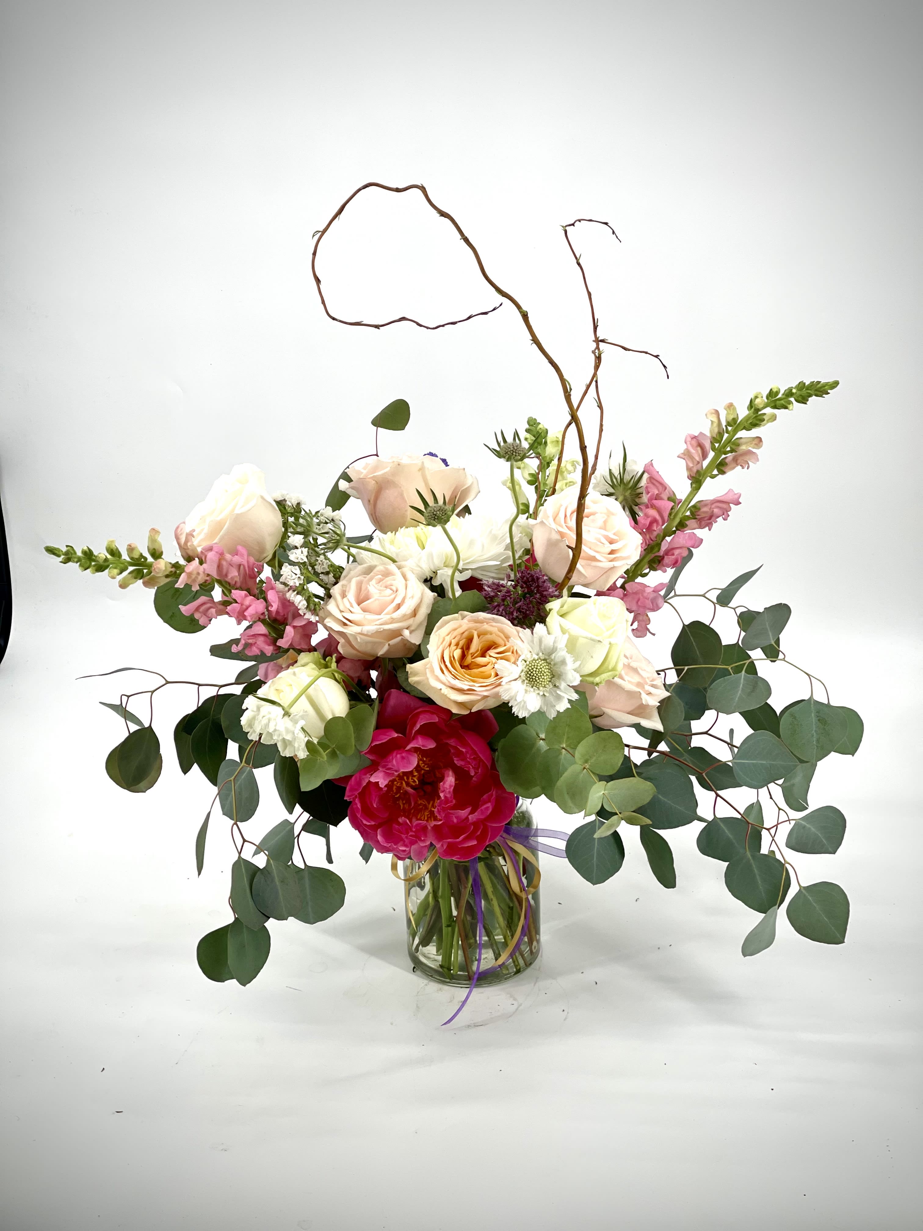 Mixed bouquet of roses, peonies, and snapdragons in a glass vase