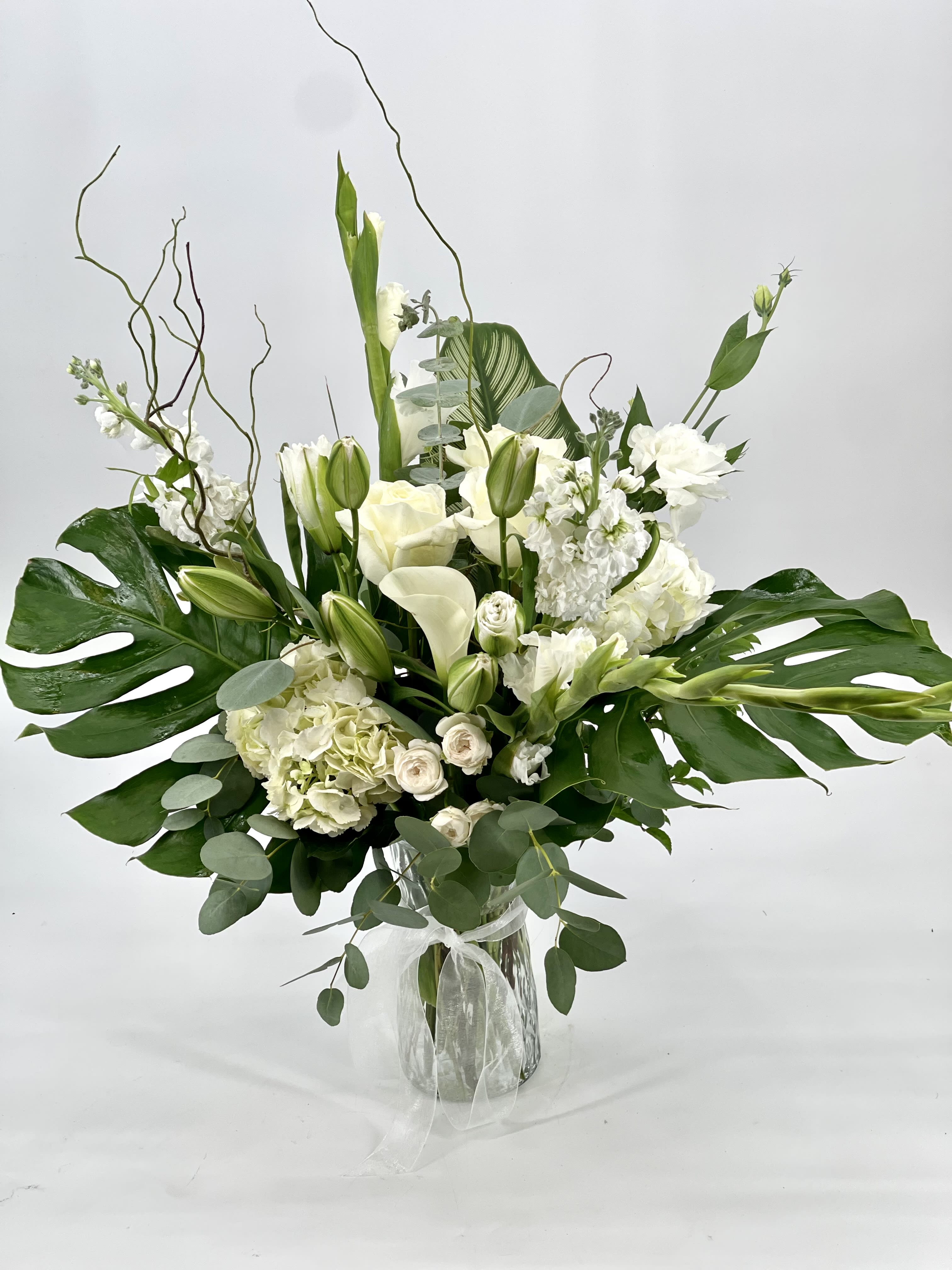 White floral arrangement in a clear glass vase with large green leaves