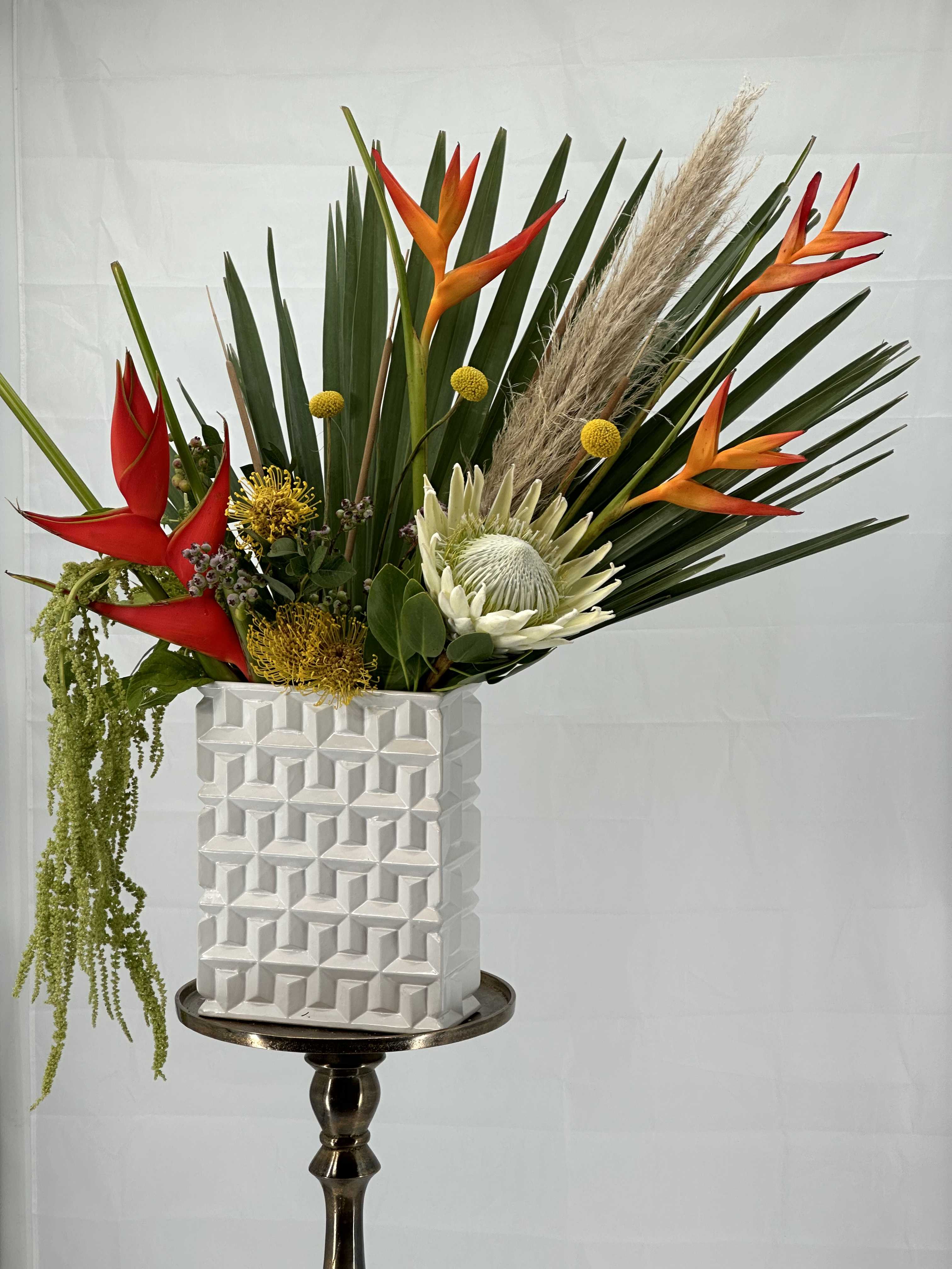 Tropical flower arrangement in a white geometric vase on a pedestal