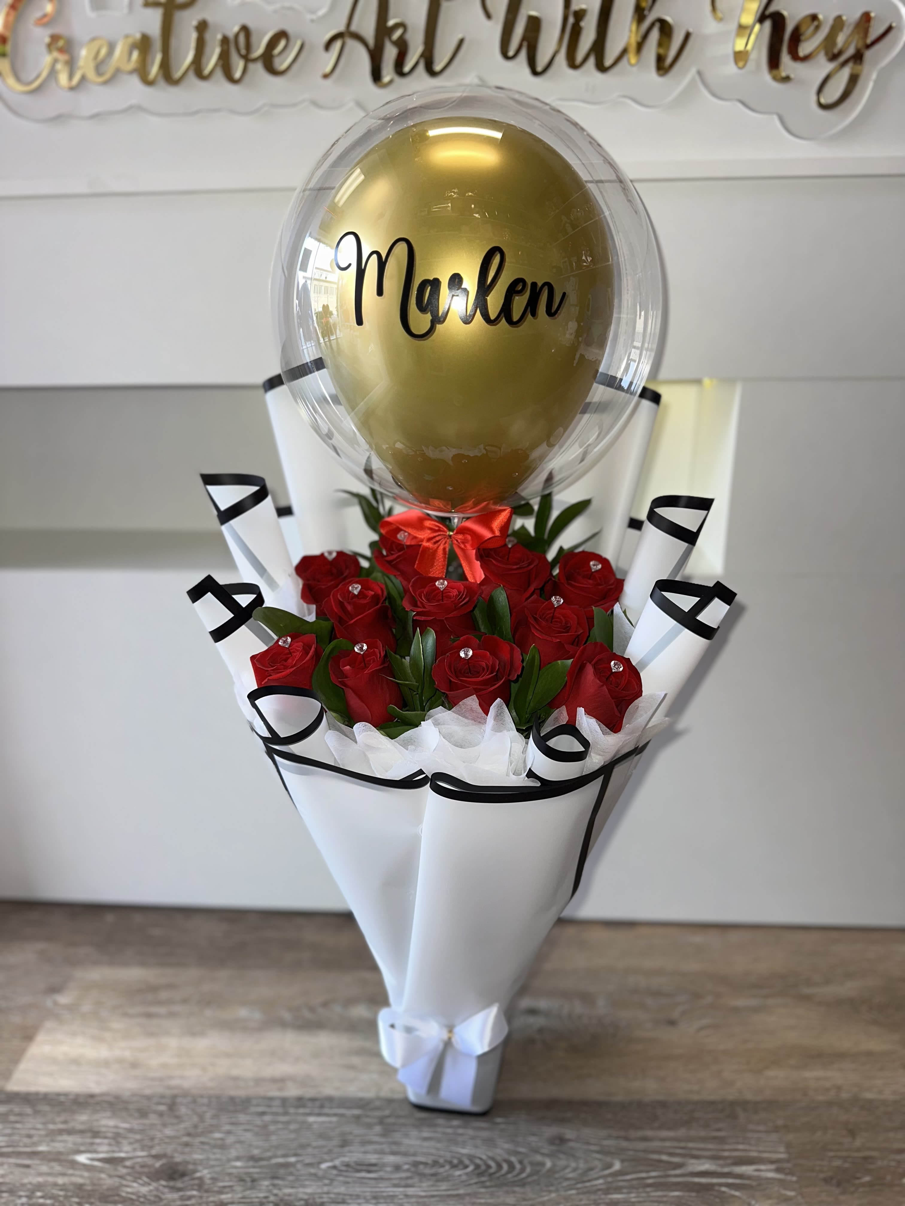 Red roses in white wrap with a gold balloon labeled Marlen
