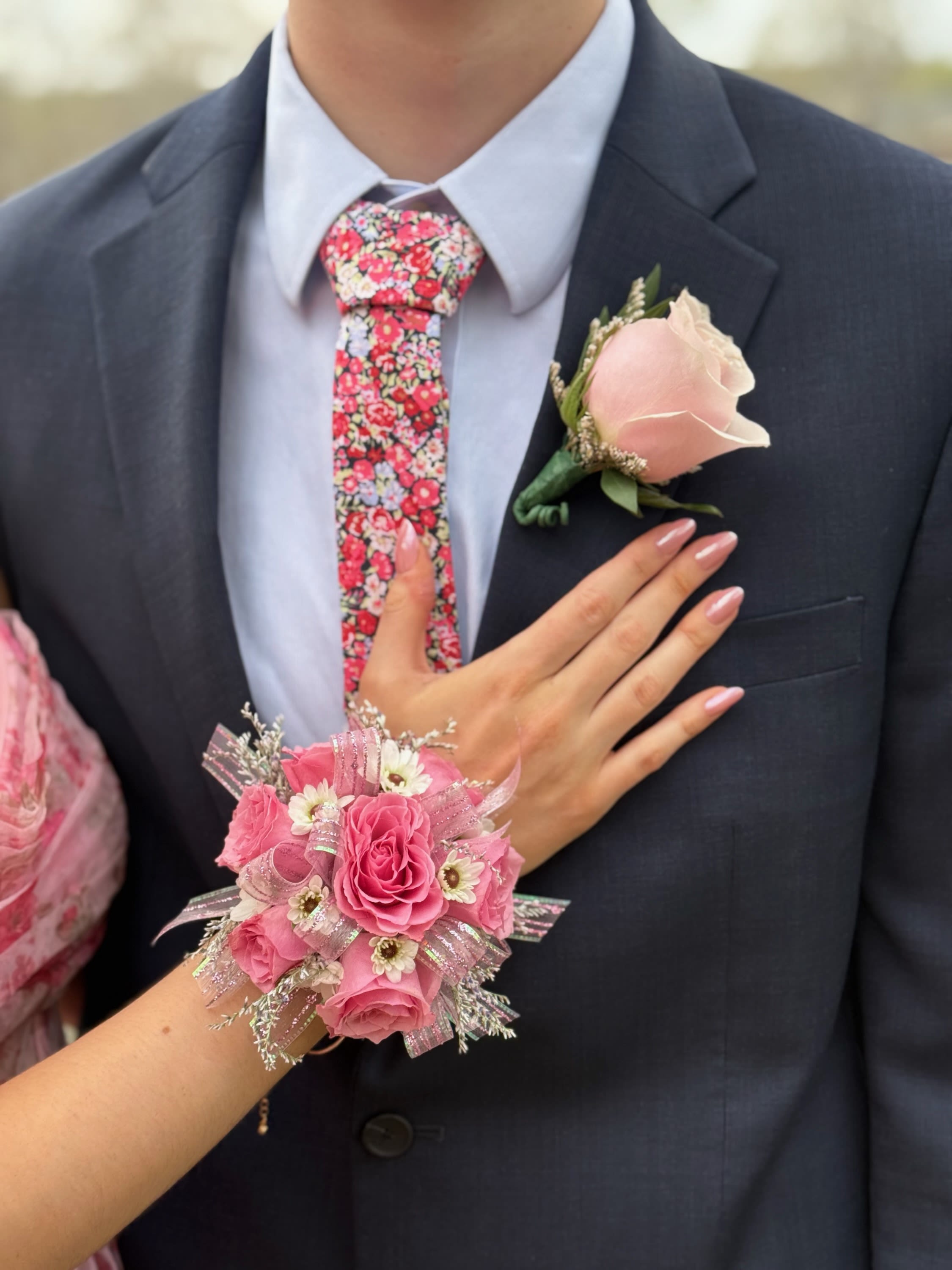 Pink rose corsage and boutonniere on a dark suit with a floral tie