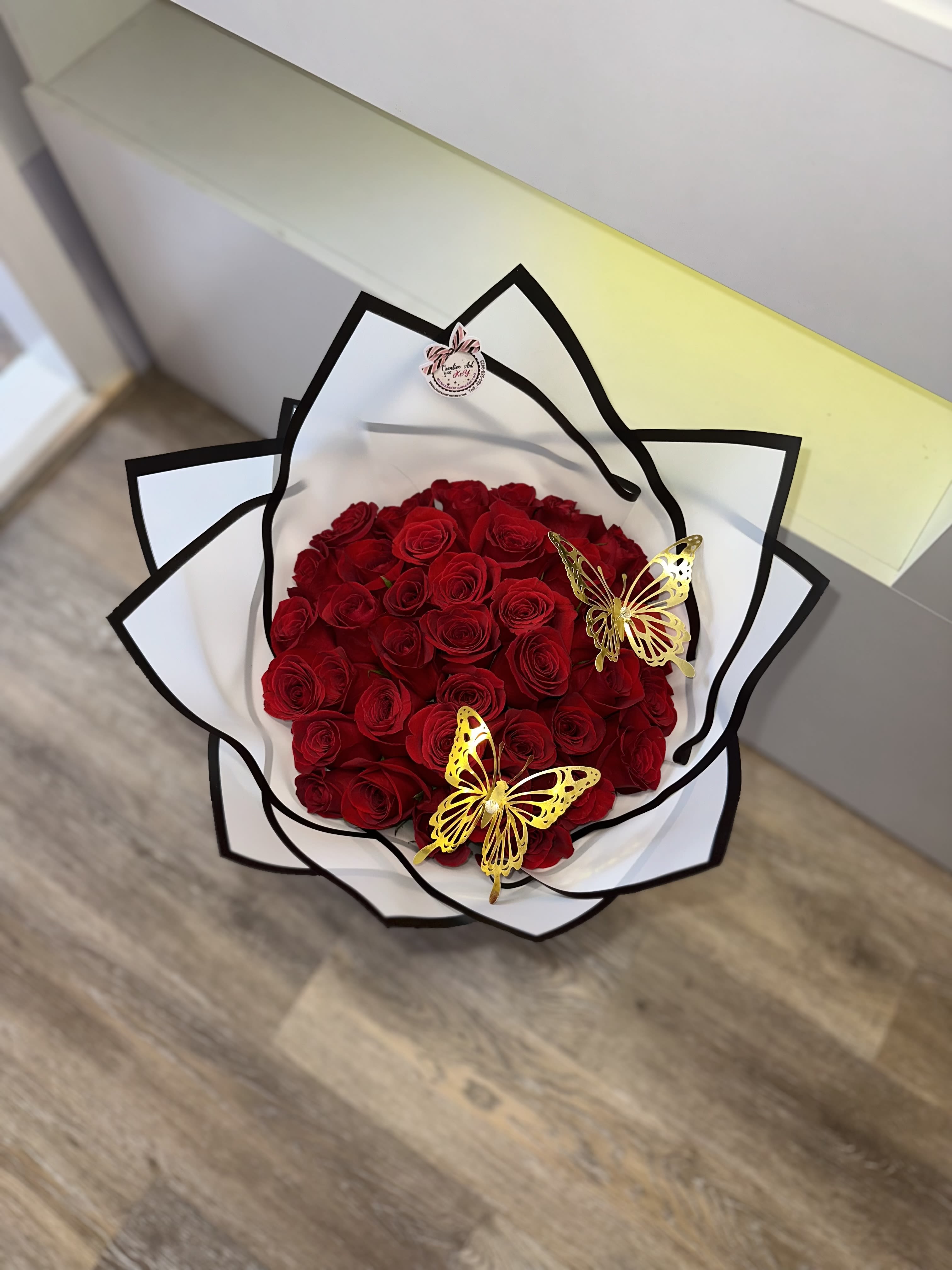 Bouquet of red roses wrapped in white paper with black trim and gold butterfly accents