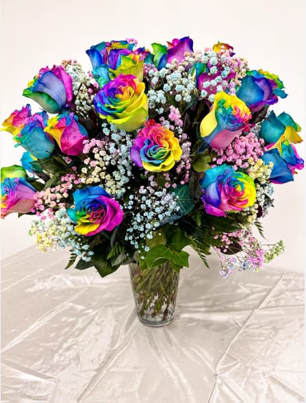 Rainbow-colored roses in a clear glass vase with baby's breath