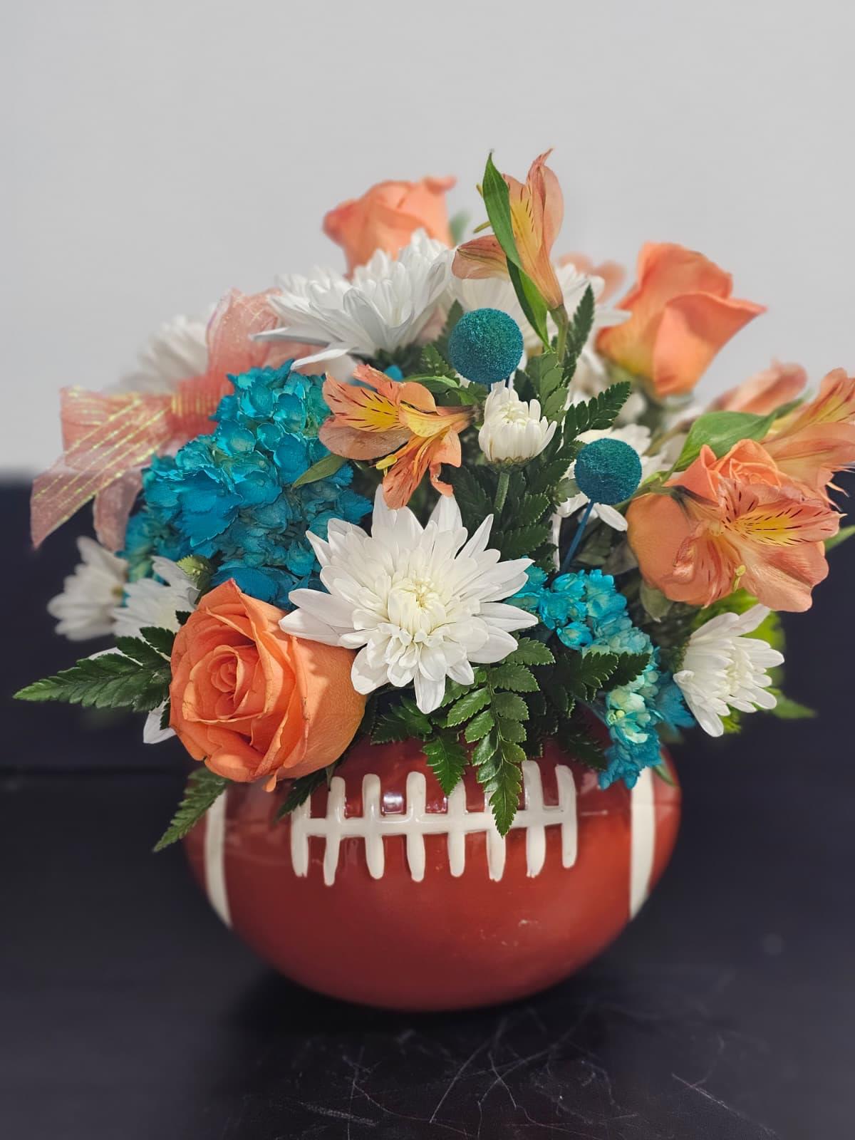 Father’s Day Touchdown Bouquet - Celebrate Dad with a winning gift he’ll never forget! Our Father’s Day Touchdown Bouquet features a vibrant mix of fresh blooms arranged in a charming football-themed keepsake container, making it the perfect centerpiece for game day or Father’s Day celebrations.   Personalize It for Dad! We can customize the flower colors to match your dad’s favorite team colors, whether he cheers for a local high school, college, or professional football team. Simply let us know his team, and we’ll create a one-of-a-kind arrangement just for him.  Designed with bright roses, chrysanthemums, hydrangea, and seasonal accent flowers, this arrangement is a great way to honor the MVP in your life.