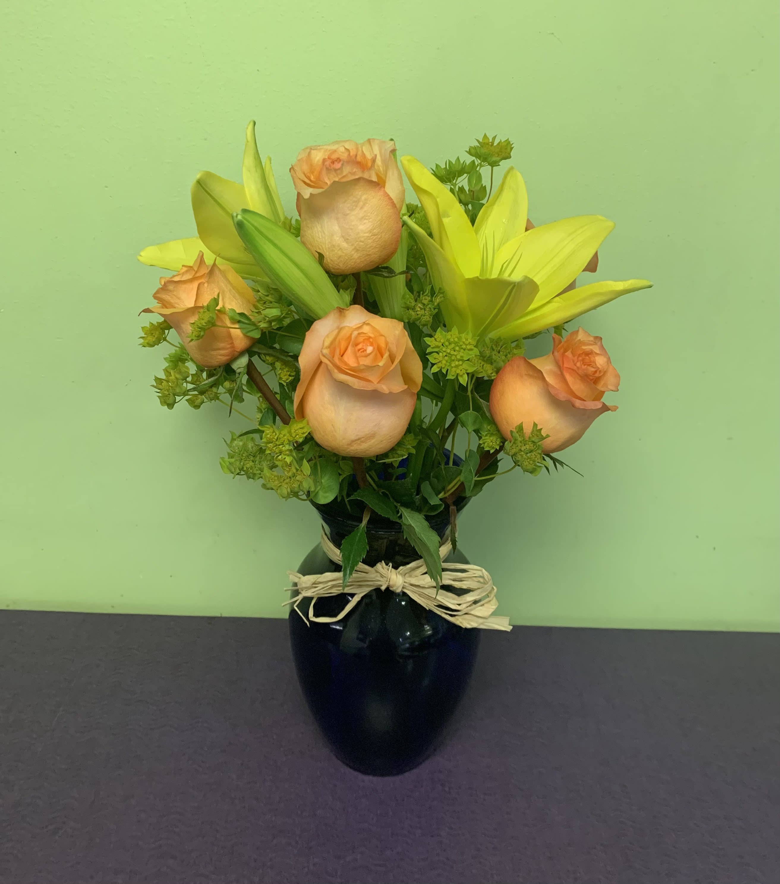 Peach roses and yellow lilies in a black vase with a raffia bow
