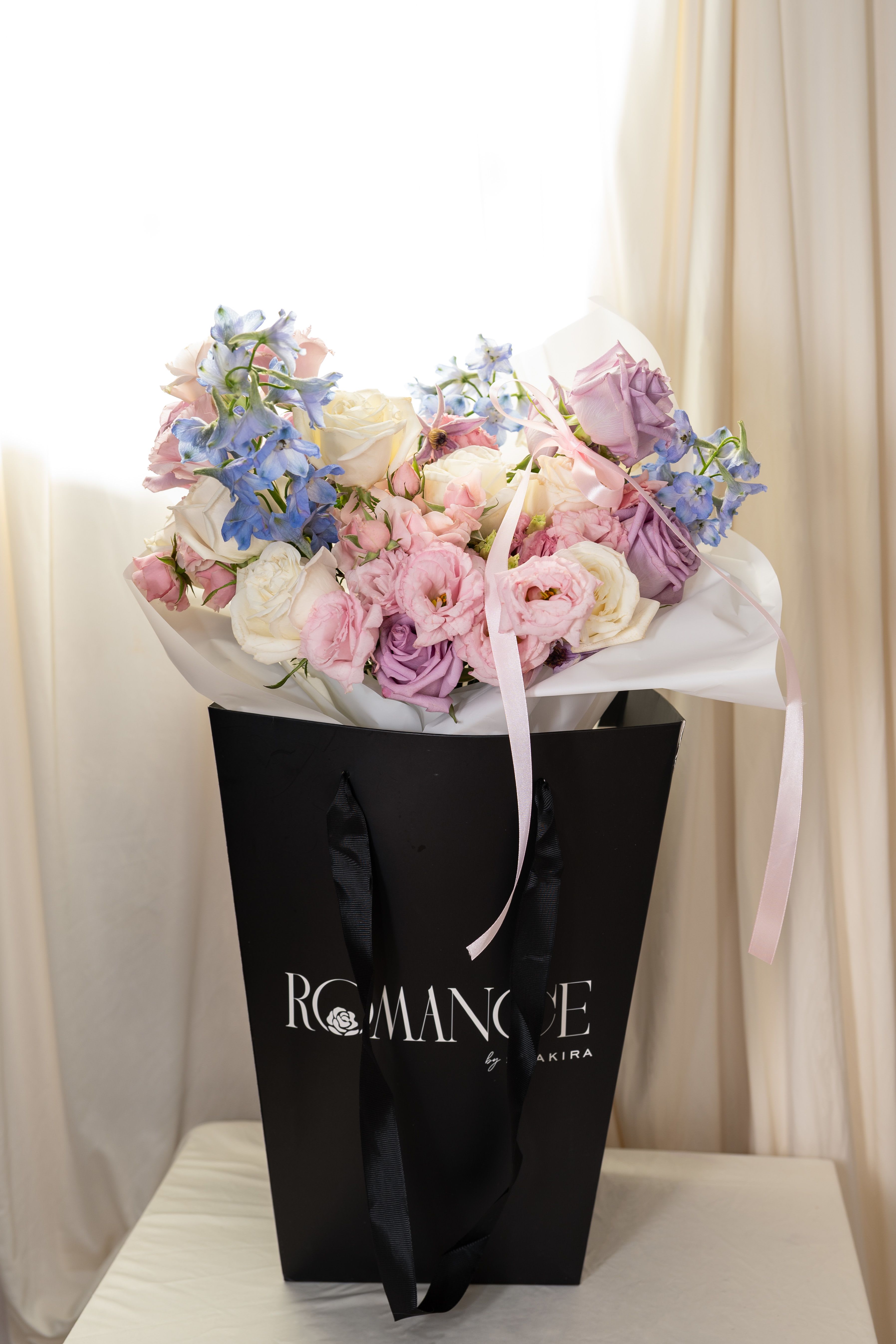 Love Song - Love Song is the most abundant bouquet in our Valentine’s Day Collection, designed to feel soft, romantic, and intentional. It features lavender and white roses, pink spray roses, lisianthus, blue delphinium, and lavender clematis in a dreamy, garden-inspired design.  Each bouquet includes a handwritten note and is lightly misted with our signature Romance perfume and a Romance by Shakira bag.  From the Valentine’s Day Collection Romance by Shakira