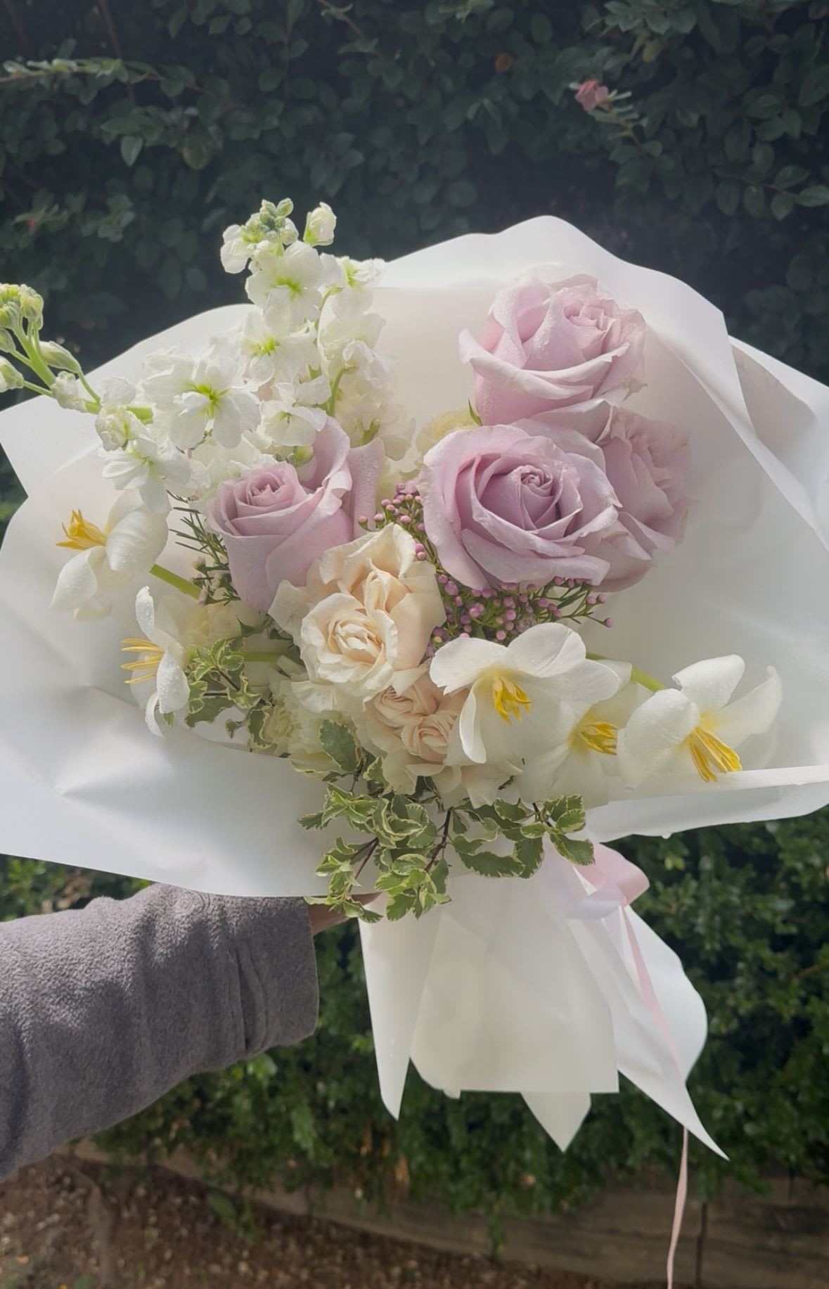 Handheld bouquet of pale pink and white flowers wrapped in white paper