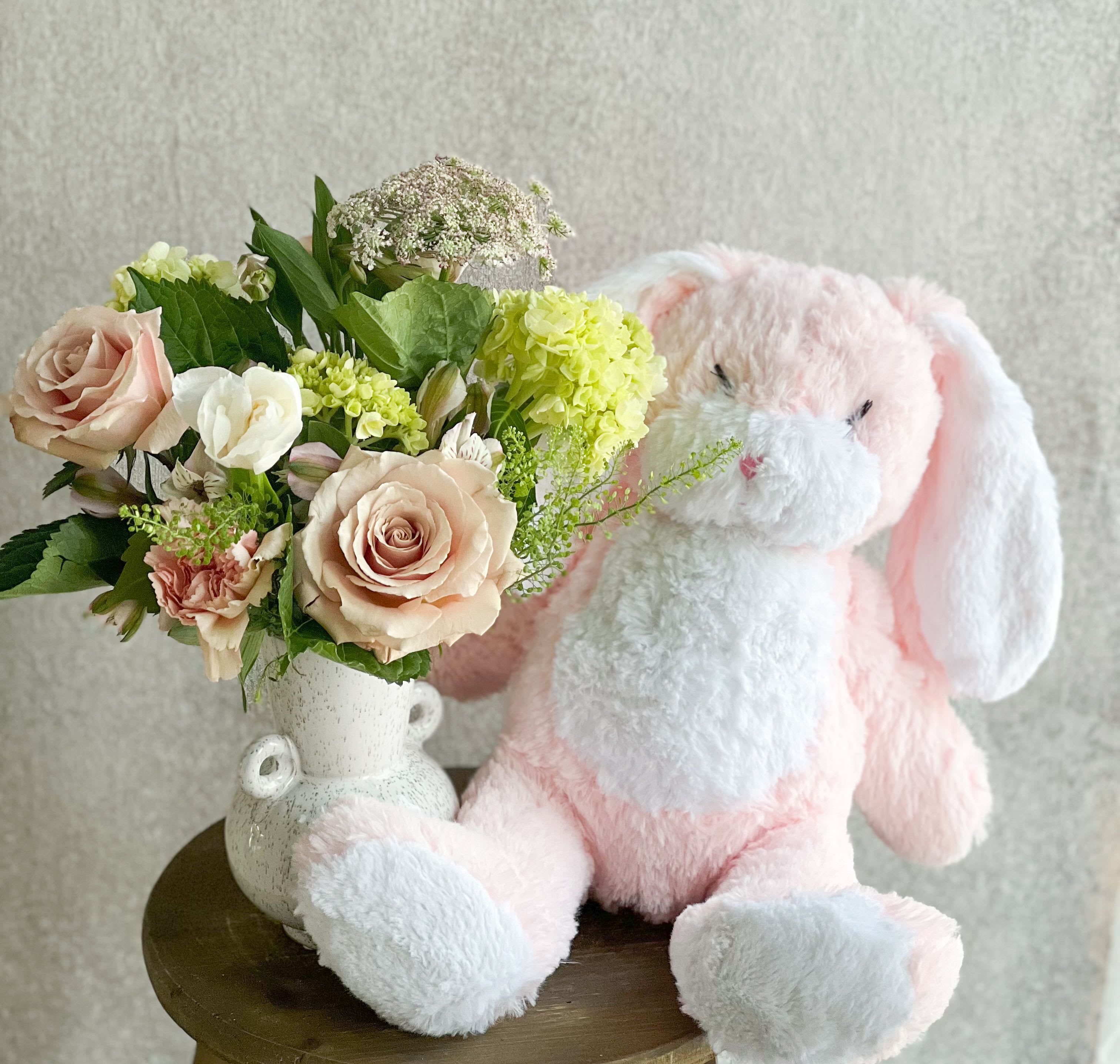 Pink plush bunny beside a vase of pale roses and mixed flowers