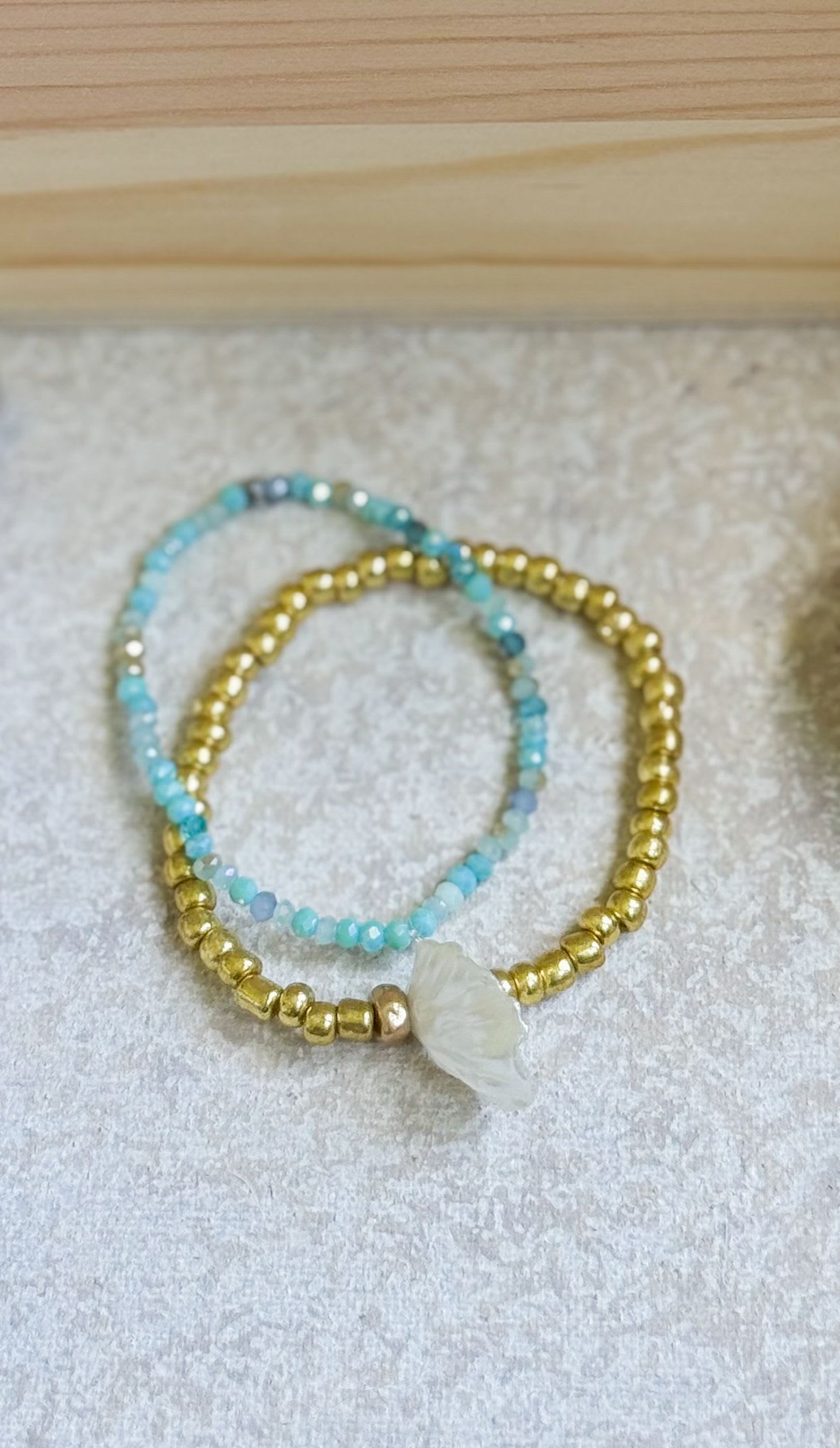 Two beaded bracelets with blue and gold beads and a white shell charm