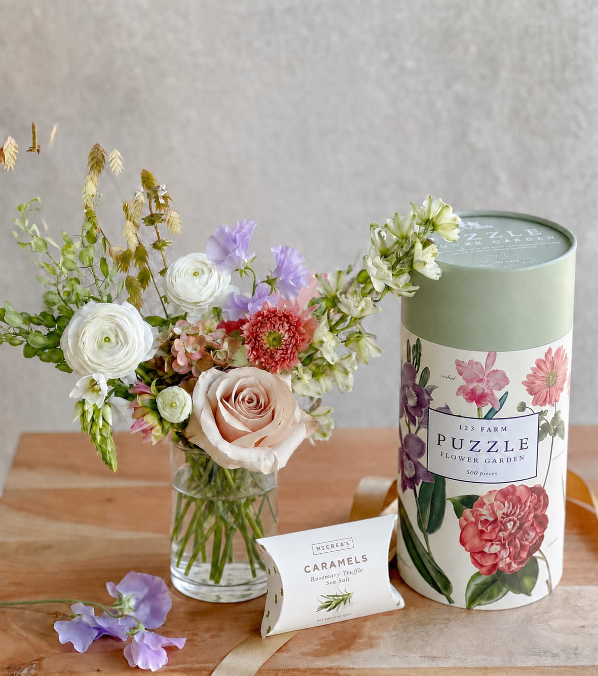 Flower arrangement in a glass vase beside a puzzle tin and caramel box