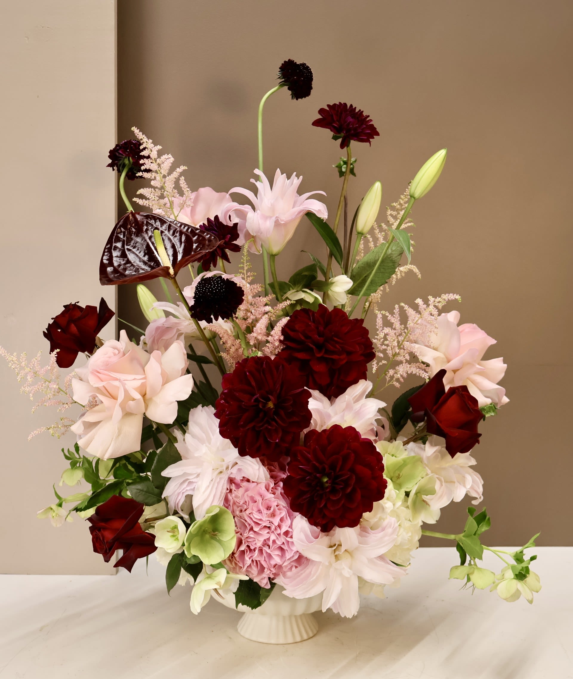 Blush &amp; Burgundy - A truly elegant, English garden inspired arrangement featuring a rich variety of premium and sophisticated blooms in tones of Deep Burgundy and soft Blush. Dahlias, Dutch Roses, Rose Lilies, Hellebores, Astilbe, Anthurium, Scabiosa, and delicate seasonal accents. Designed in a classic pedestal vase, this lush composition is a work of art.