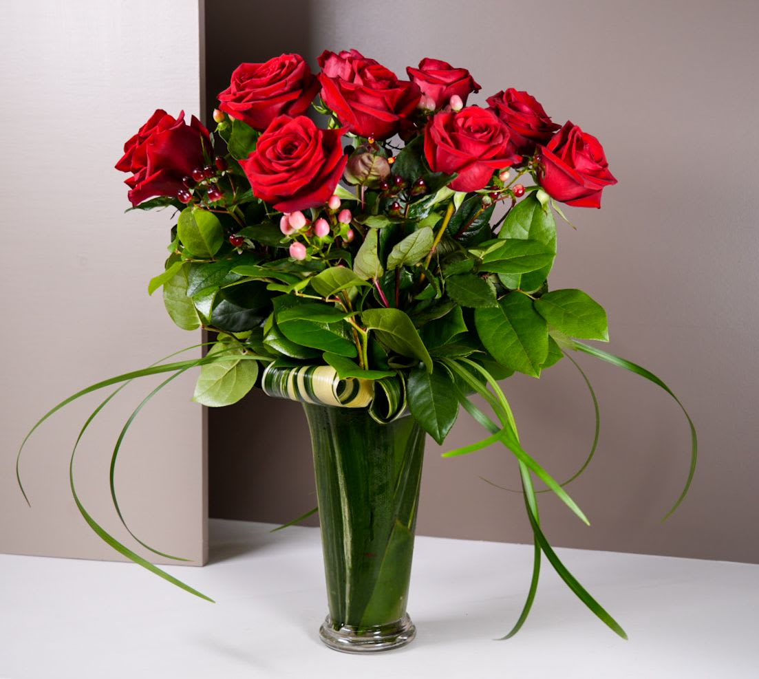 Red roses arranged in a tall glass vase with greenery
