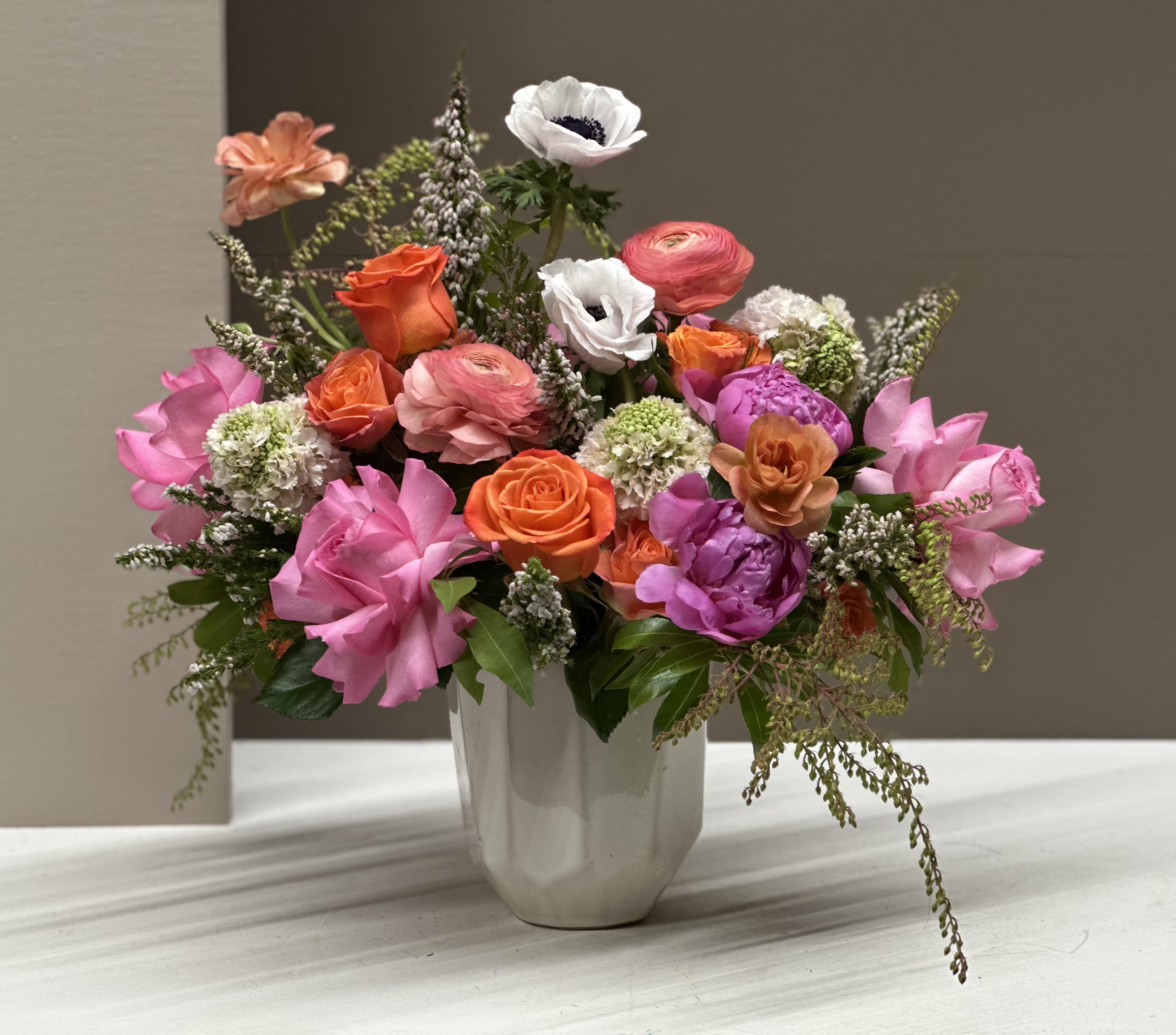 Mixed pink, orange, and white flowers arranged in a white vase