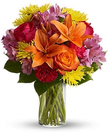 Mixed bouquet of orange lilies, roses, and colorful daisies in a glass vase