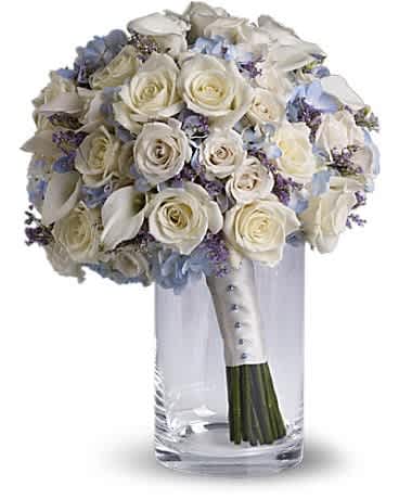 White rose bouquet with blue accents in a clear glass vase