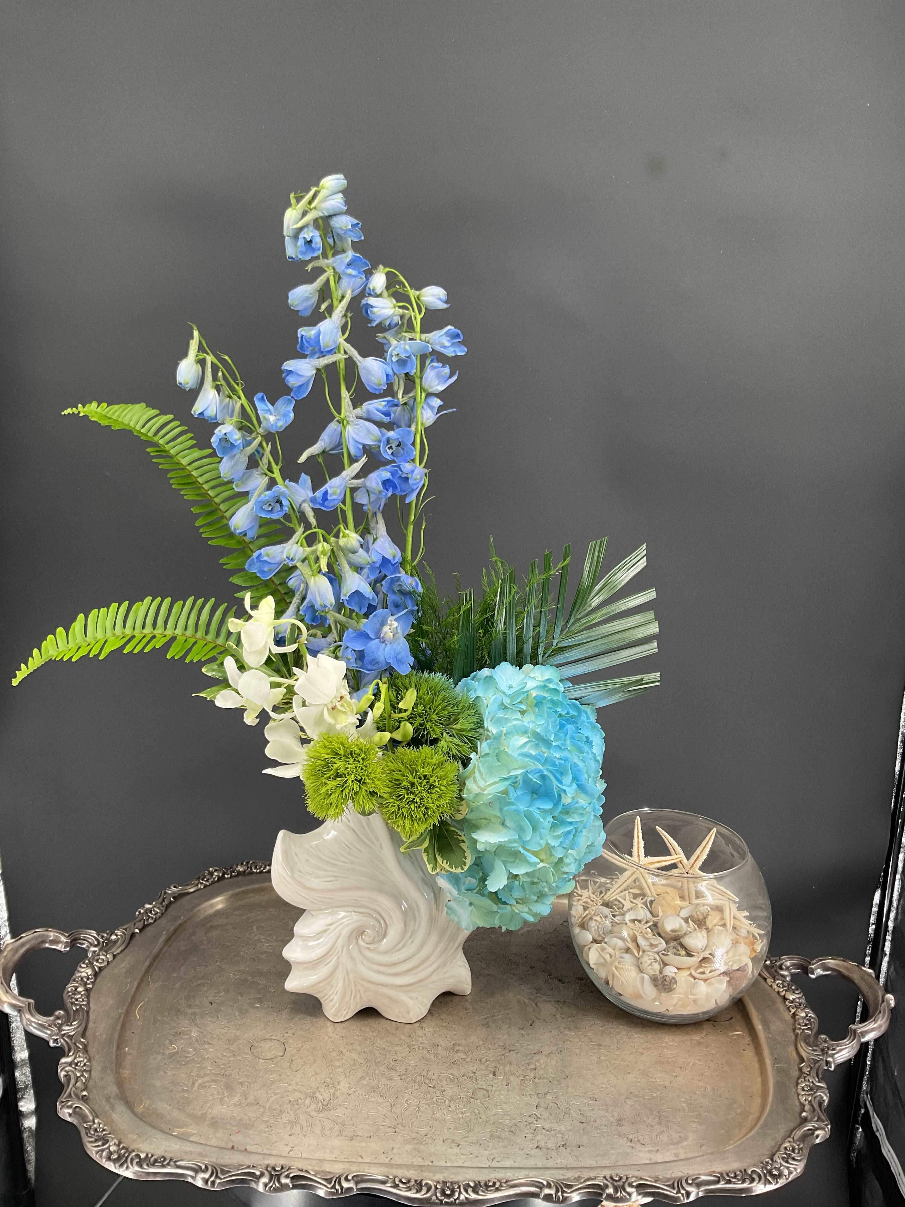 Blue and white floral arrangement in a white vase with green accents