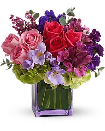 Mixed bouquet of roses, hydrangeas, and purple flowers in a square glass vase