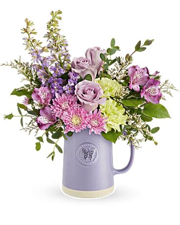 Lavender and pink flowers arranged in a purple pitcher vase