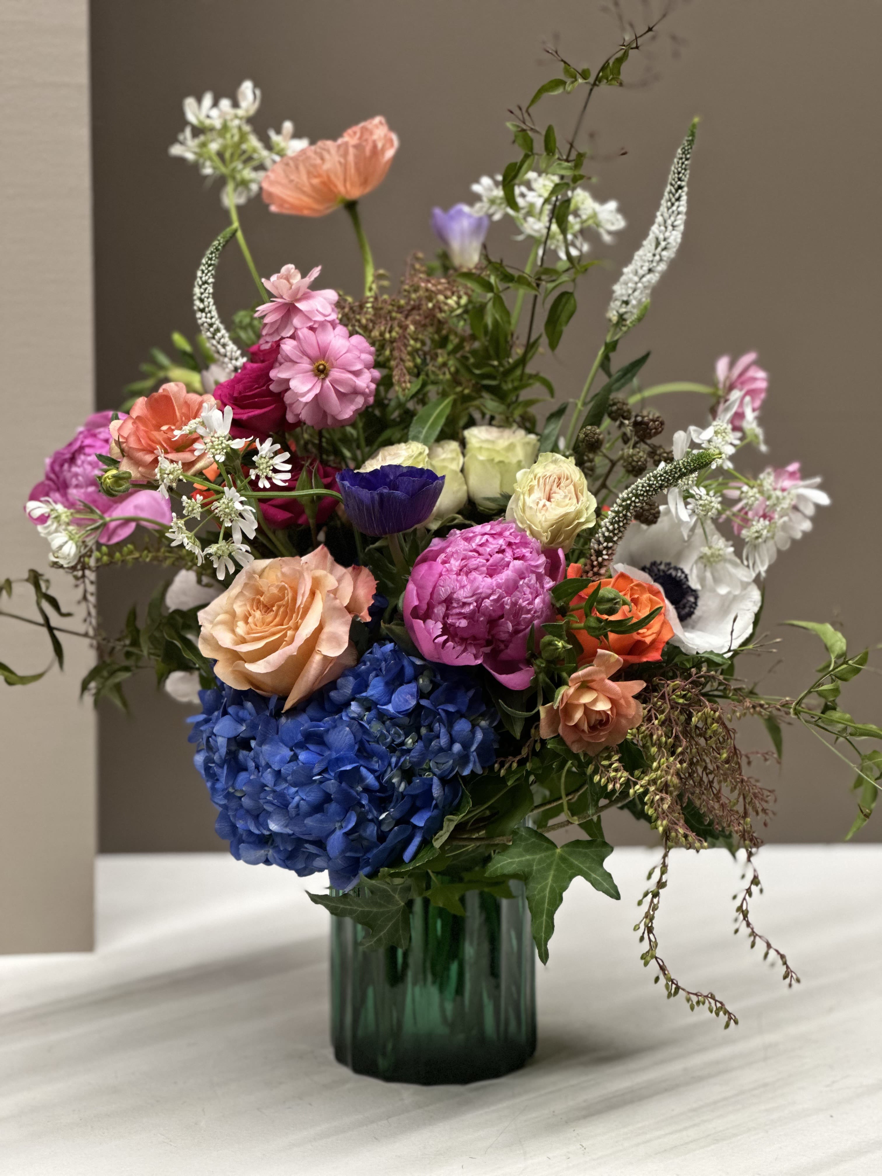 Mixed bouquet in a green glass vase with blue hydrangea and pink, peach, and white blooms