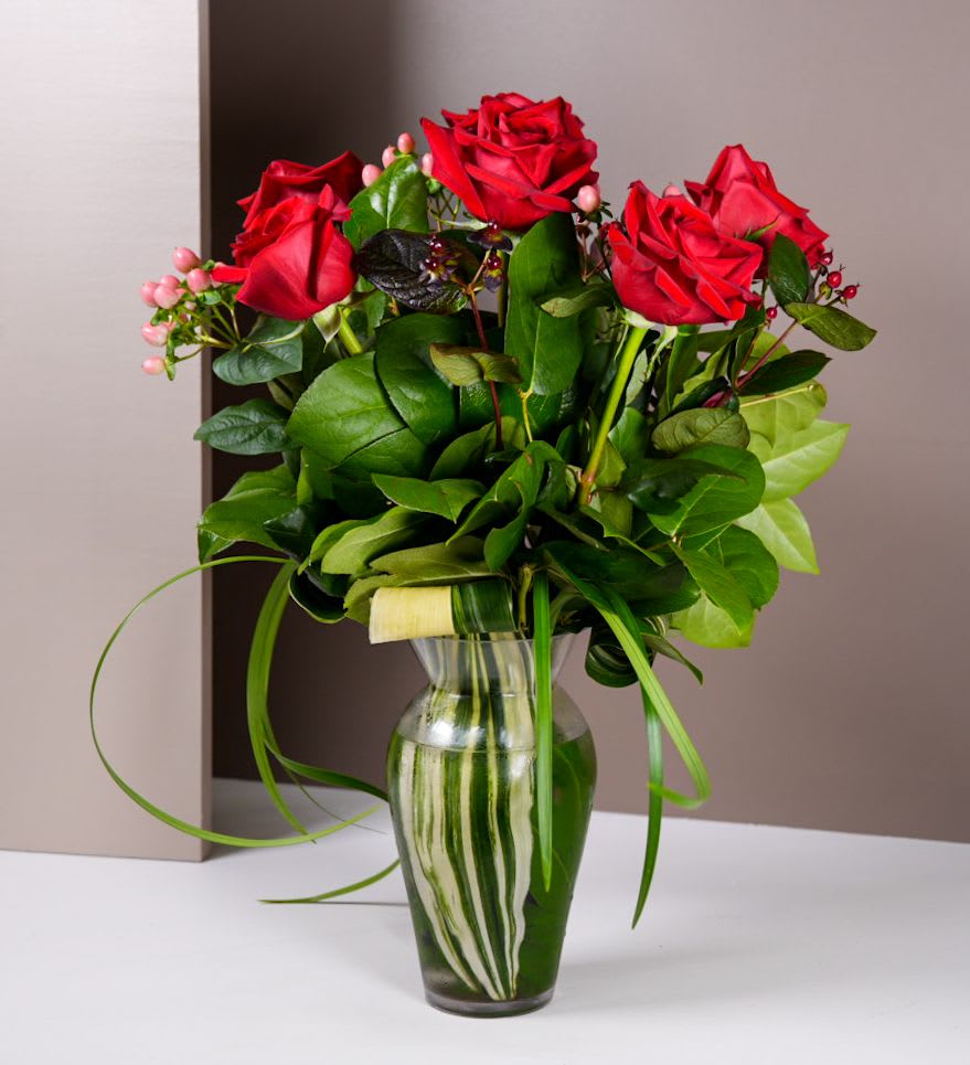 Red roses arranged in a clear glass vase with green foliage