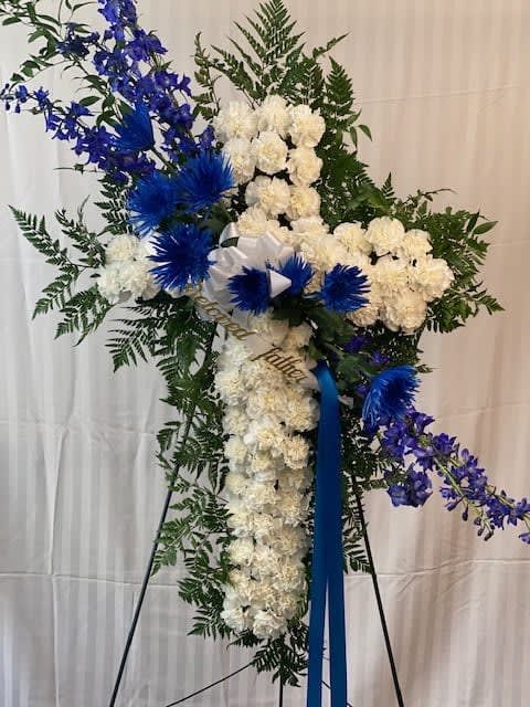 Standing floral spray with white flowers, blue accents, and a ribbon on an easel