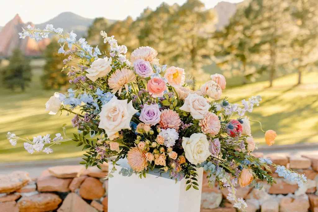 Pastel floral arrangement with roses and daisies in a white pedestal vase