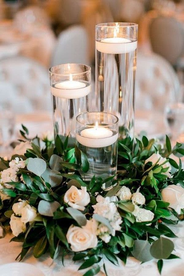 White roses and greenery around three glass candle holders