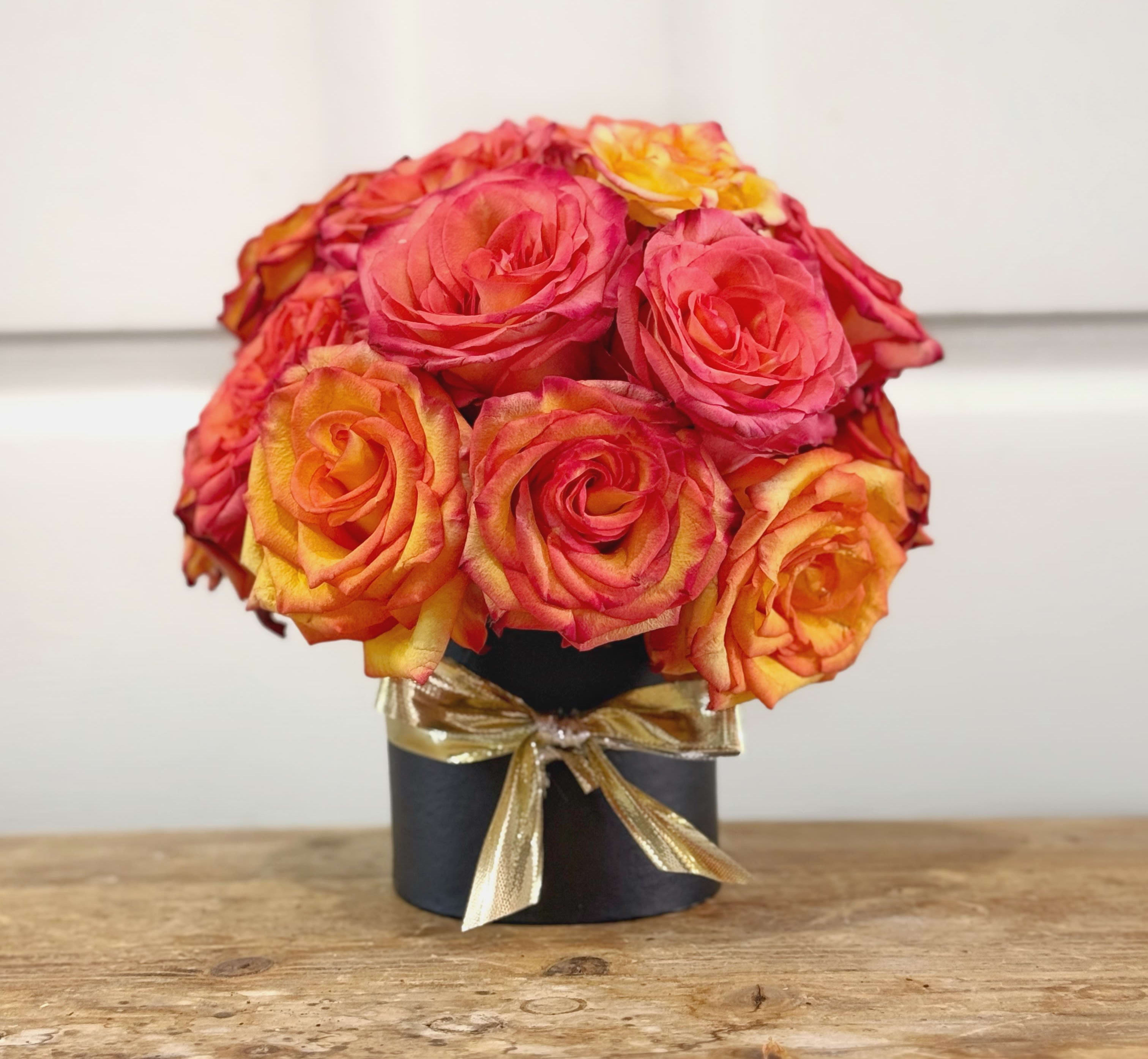 Bouquet of pink and orange roses in a black box tied with a gold ribbon