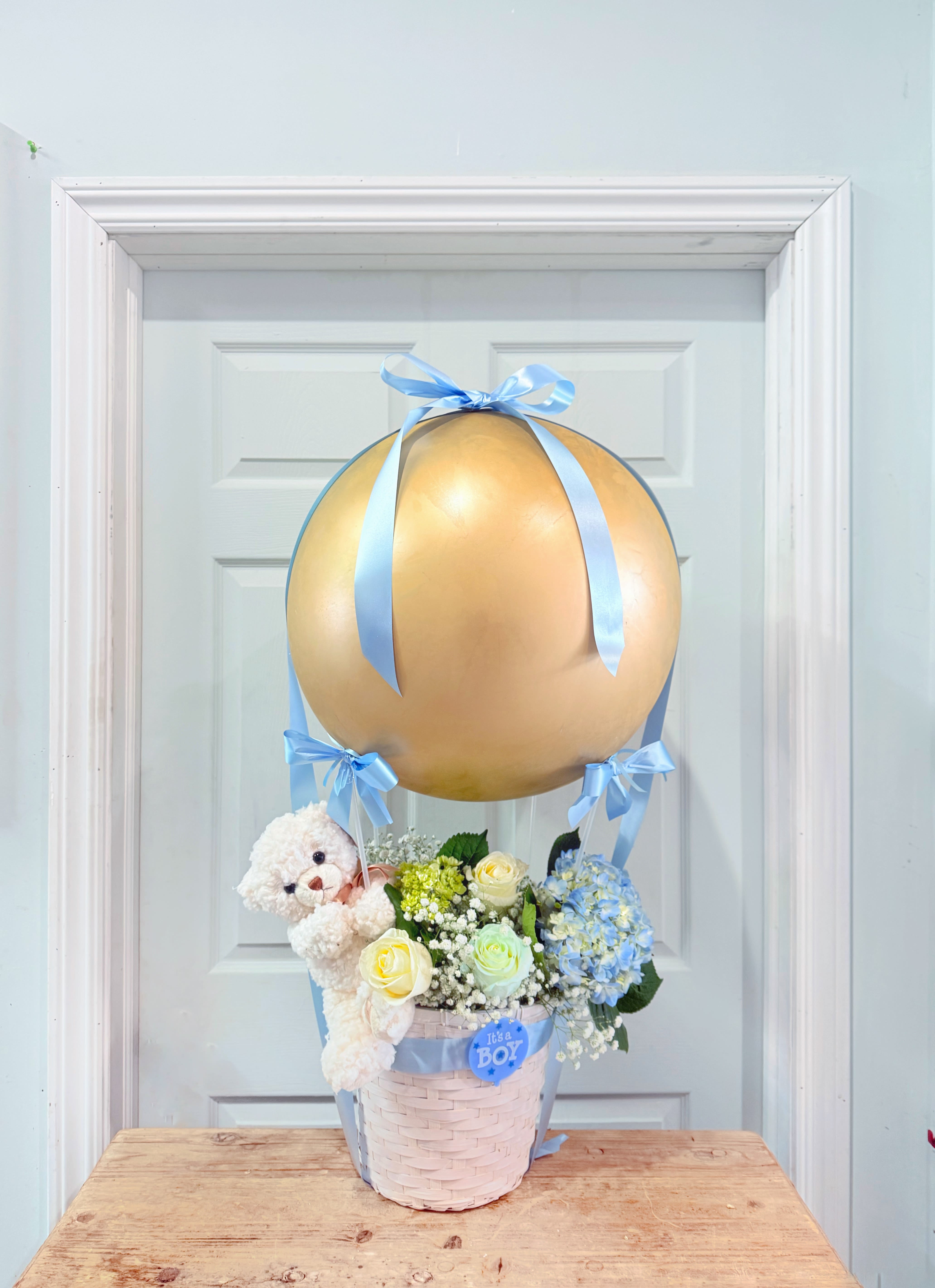 Baby gift basket with flowers, teddy bear, and gold balloon