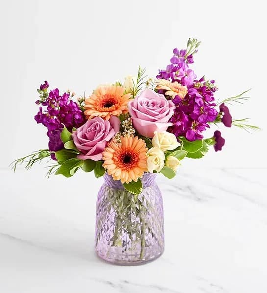 Pink roses and orange gerbera daisies in a purple glass vase