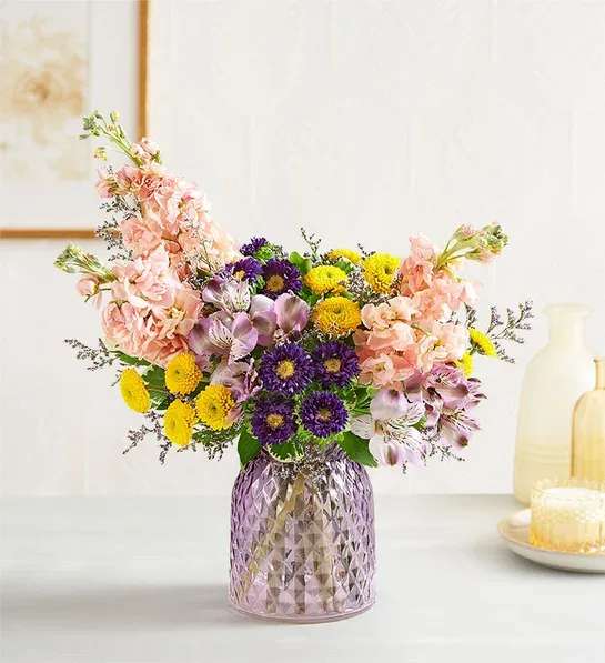 Mixed bouquet in a purple glass vase with pink, yellow, and purple flowers