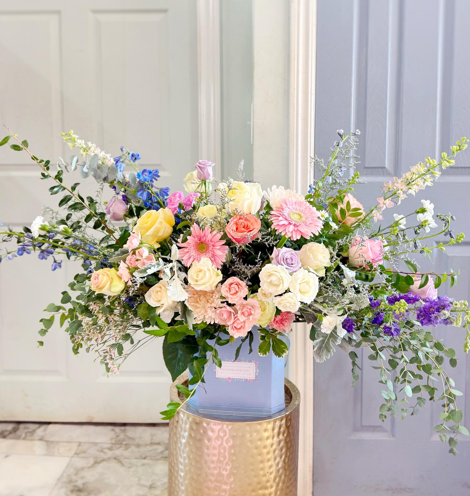 Large pastel bouquet with roses, gerbera daisies, and delphinium in a blue box