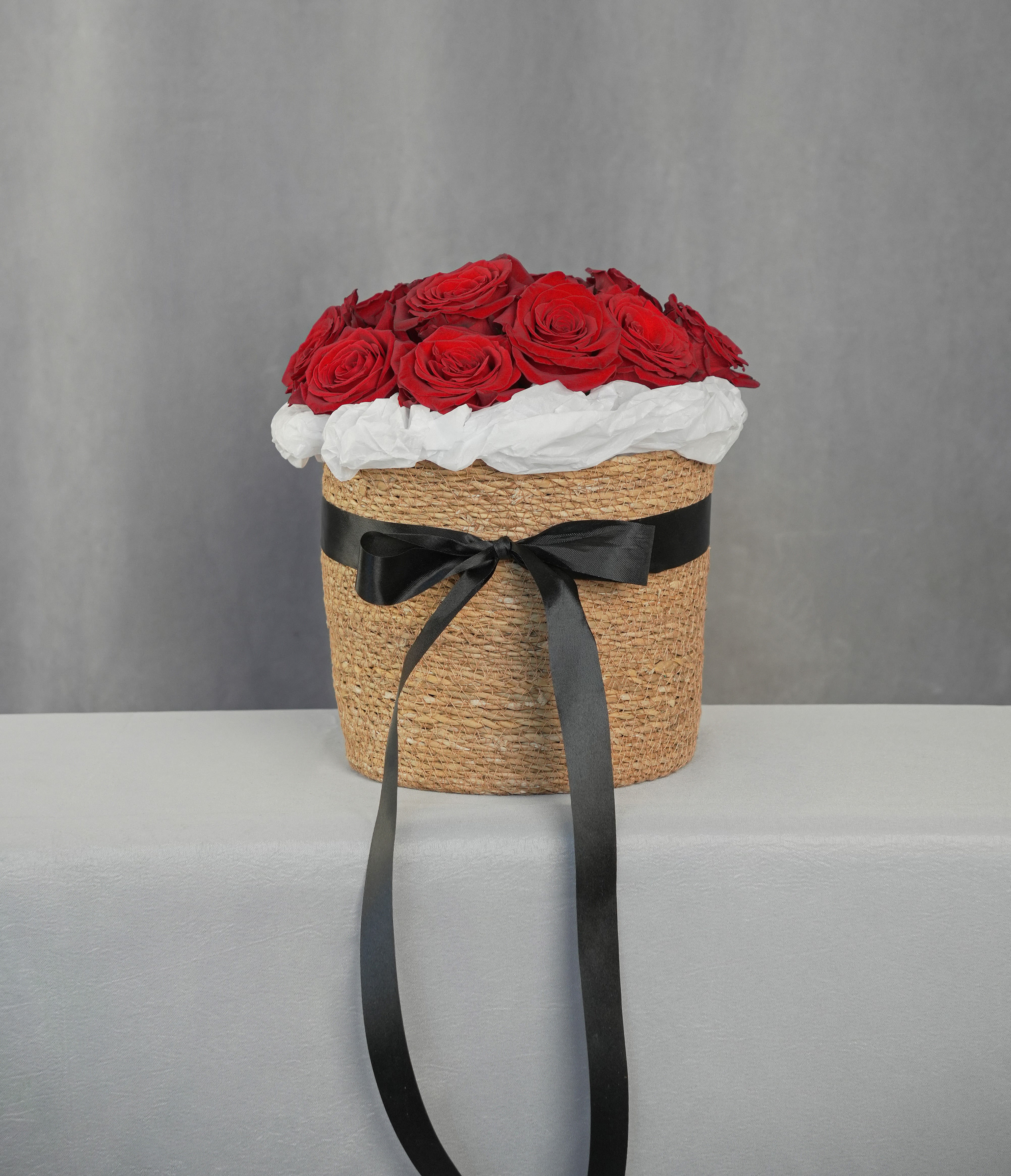 Red roses arranged in a woven hatbox with a black ribbon