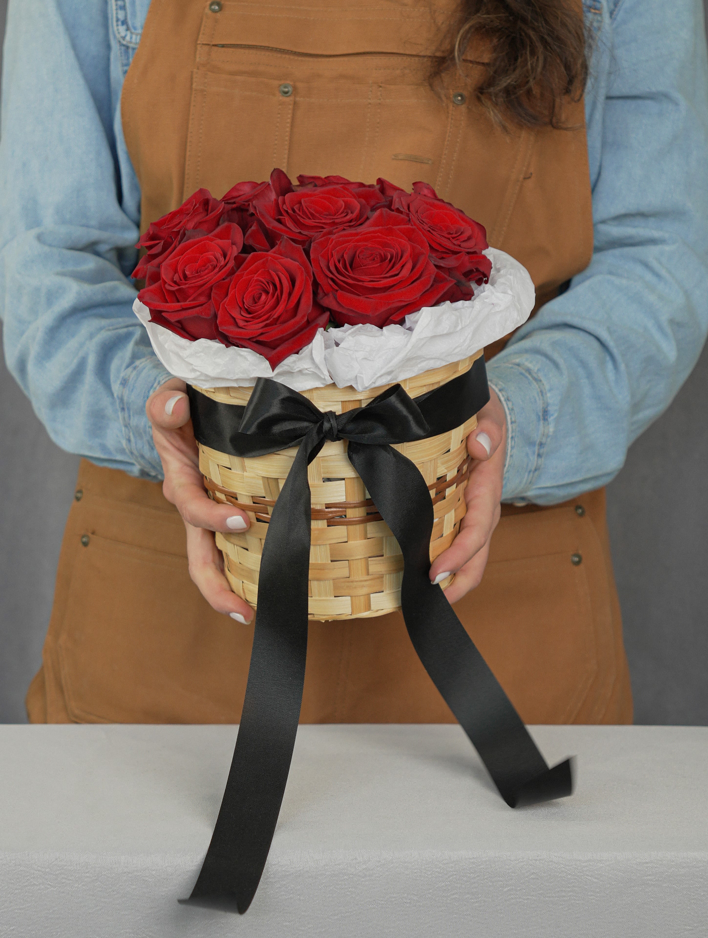 Basket of red roses wrapped with white paper and a black ribbon