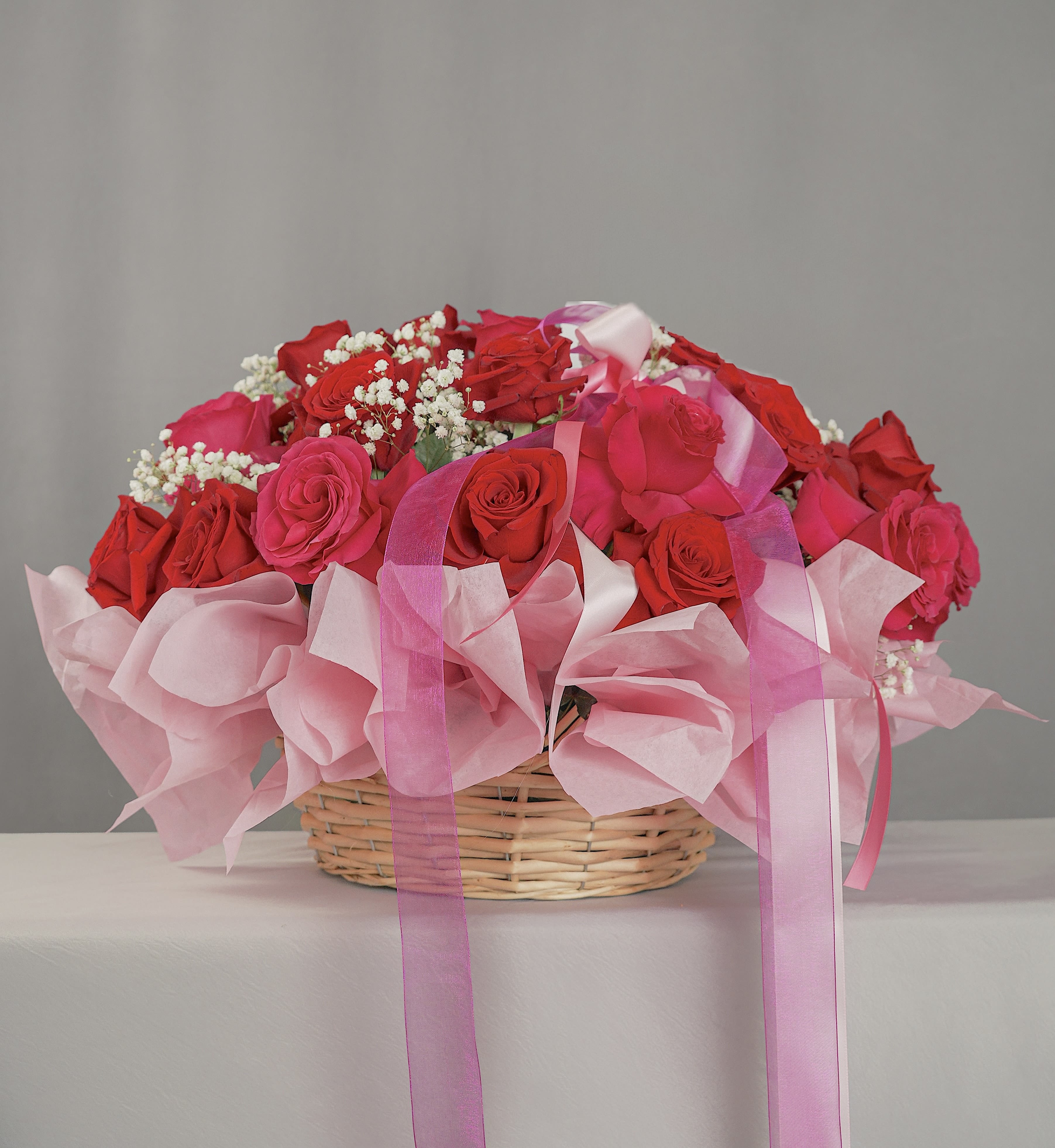 Basket of red and pink roses with baby’s breath and pink ribbons