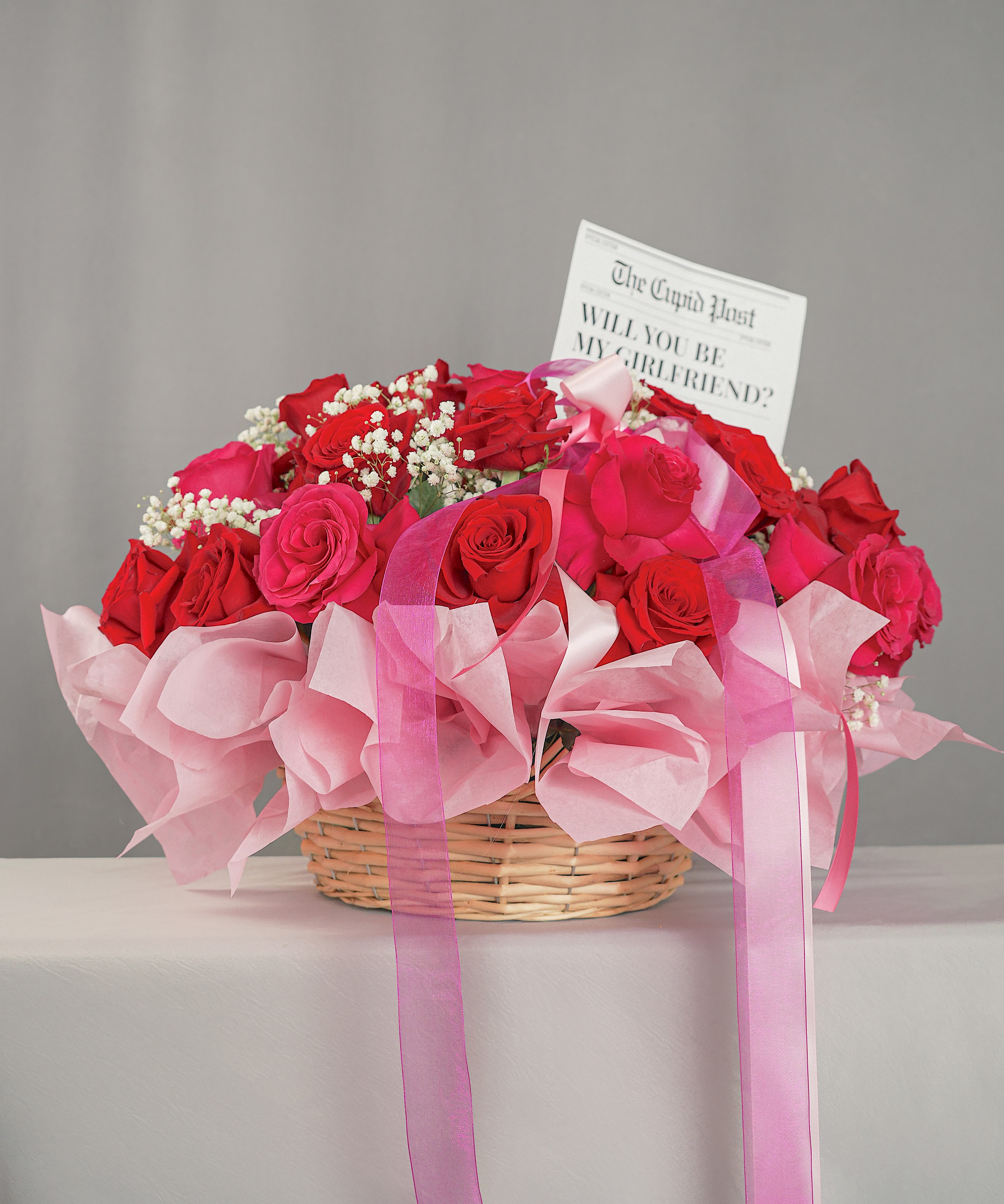 Basket of red and pink roses with a card and pink ribbon