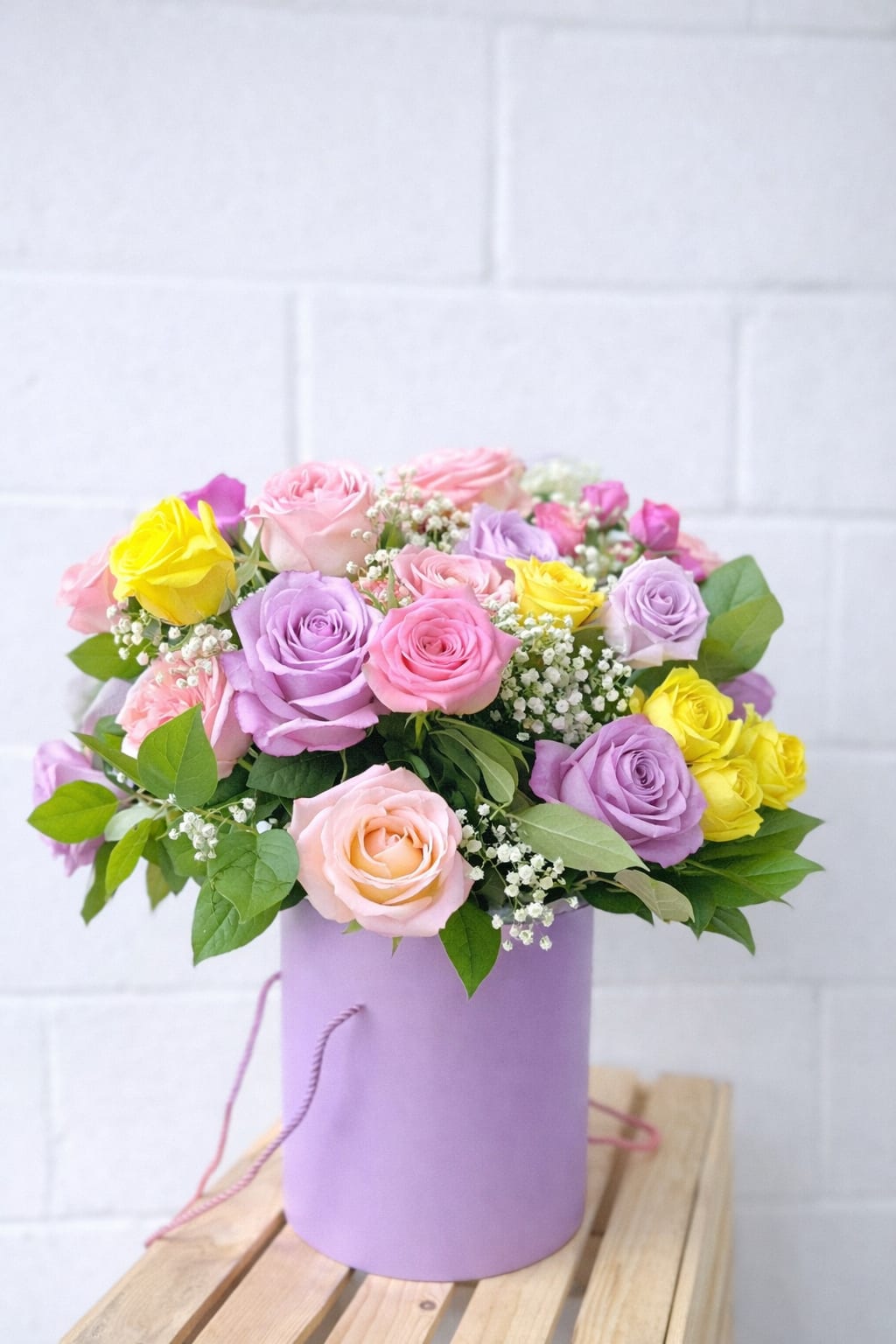 Pastel pink, lavender, and yellow roses with baby’s breath in a lavender hatbox container