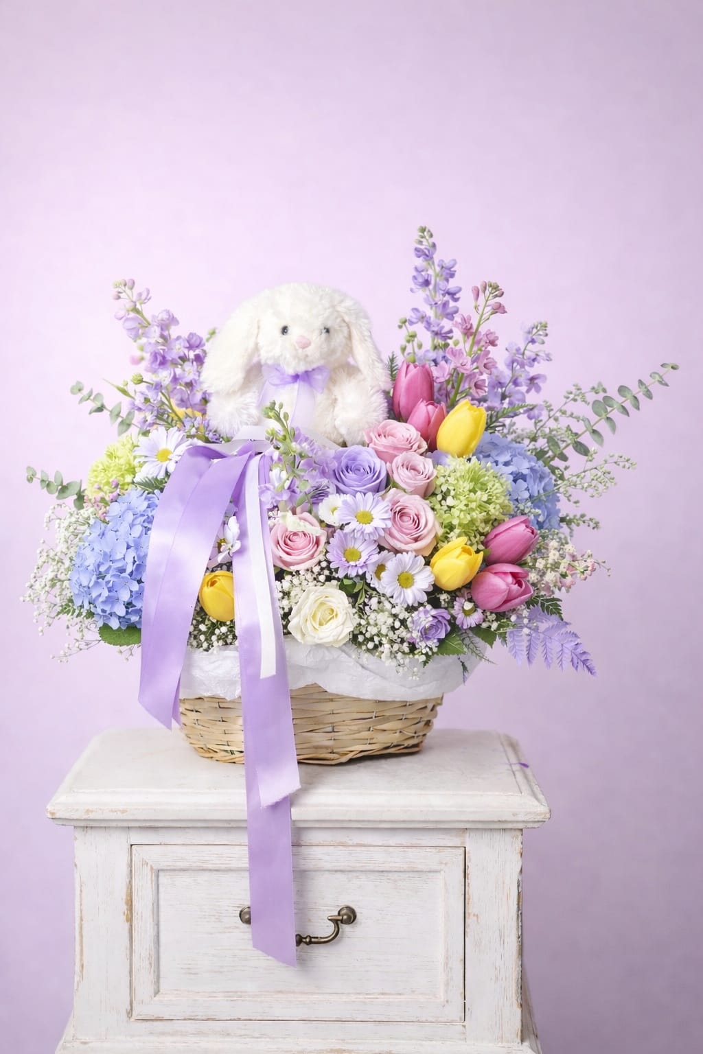 Easter Garden - A charming Easter basket featuring a mix of roses, tulips, hydrangeas, and seasonal blooms in soft mixed colors, beautifully arranged with a sweet Easter bunny plush for an extra festive touch.