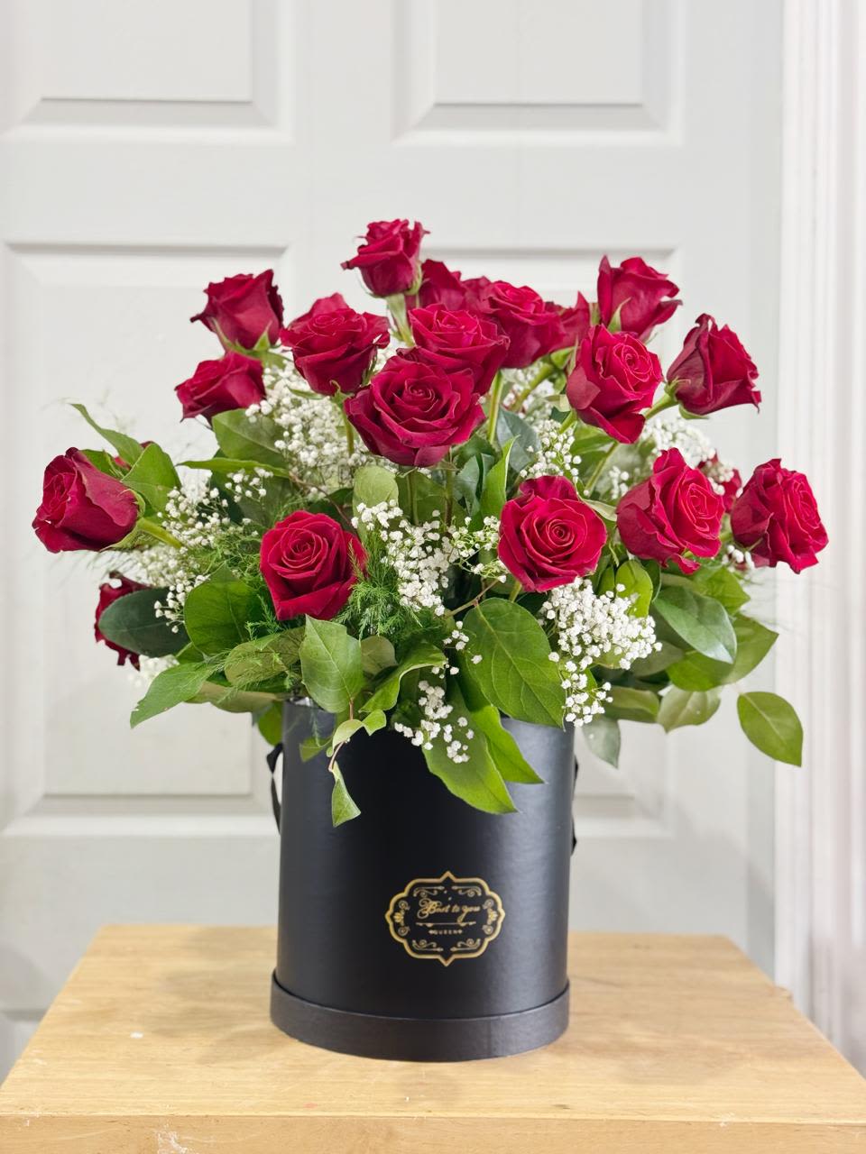 Red roses arranged in a black hat box with baby's breath