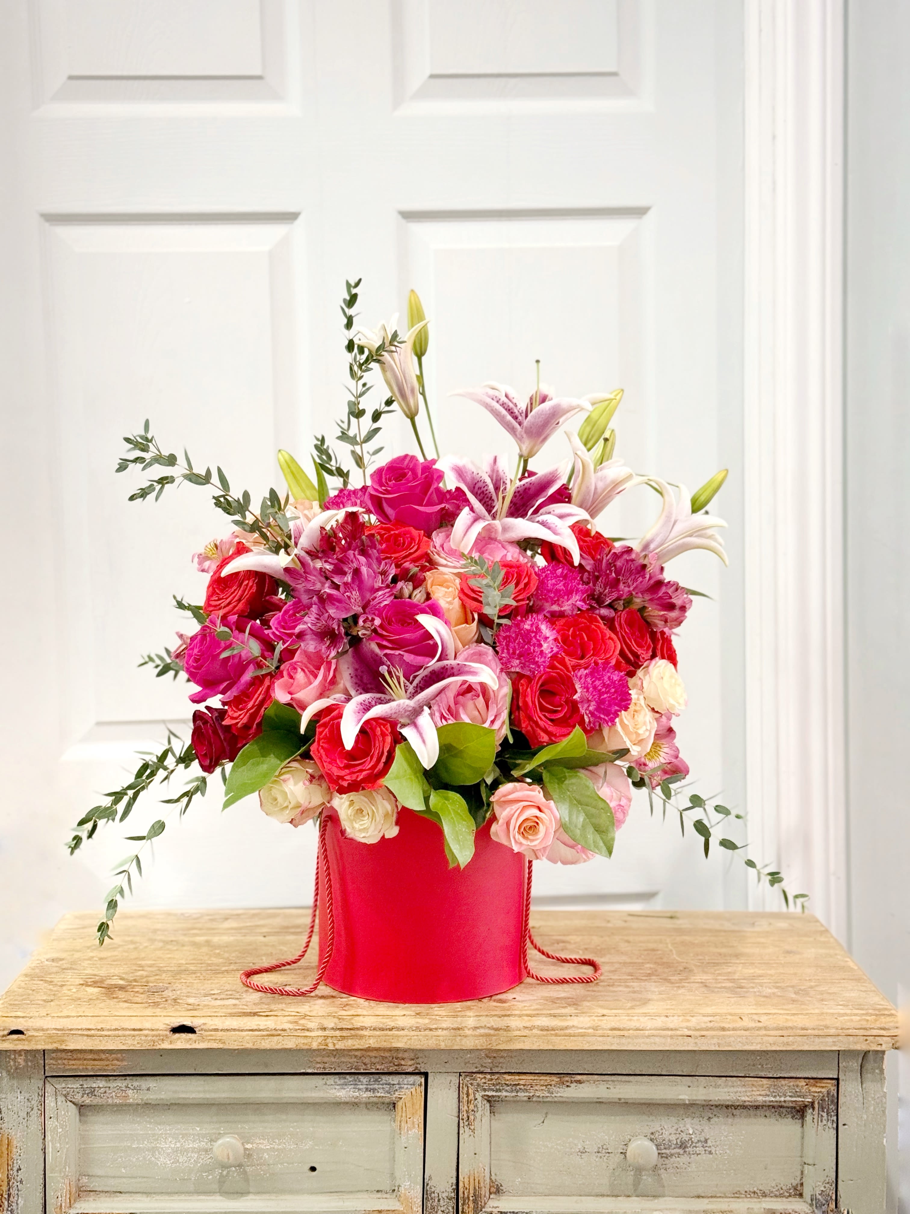 Pink and red floral arrangement in a red hatbox