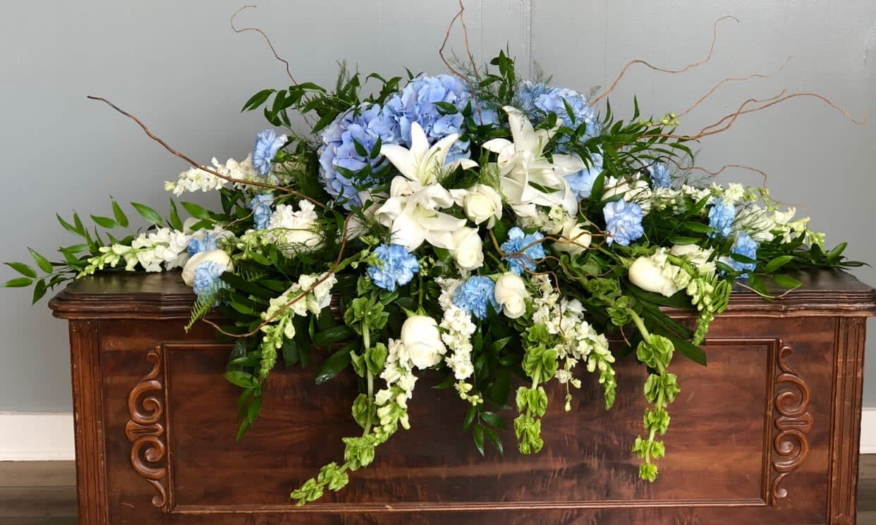 Large blue and white floral arrangement on a wooden casket