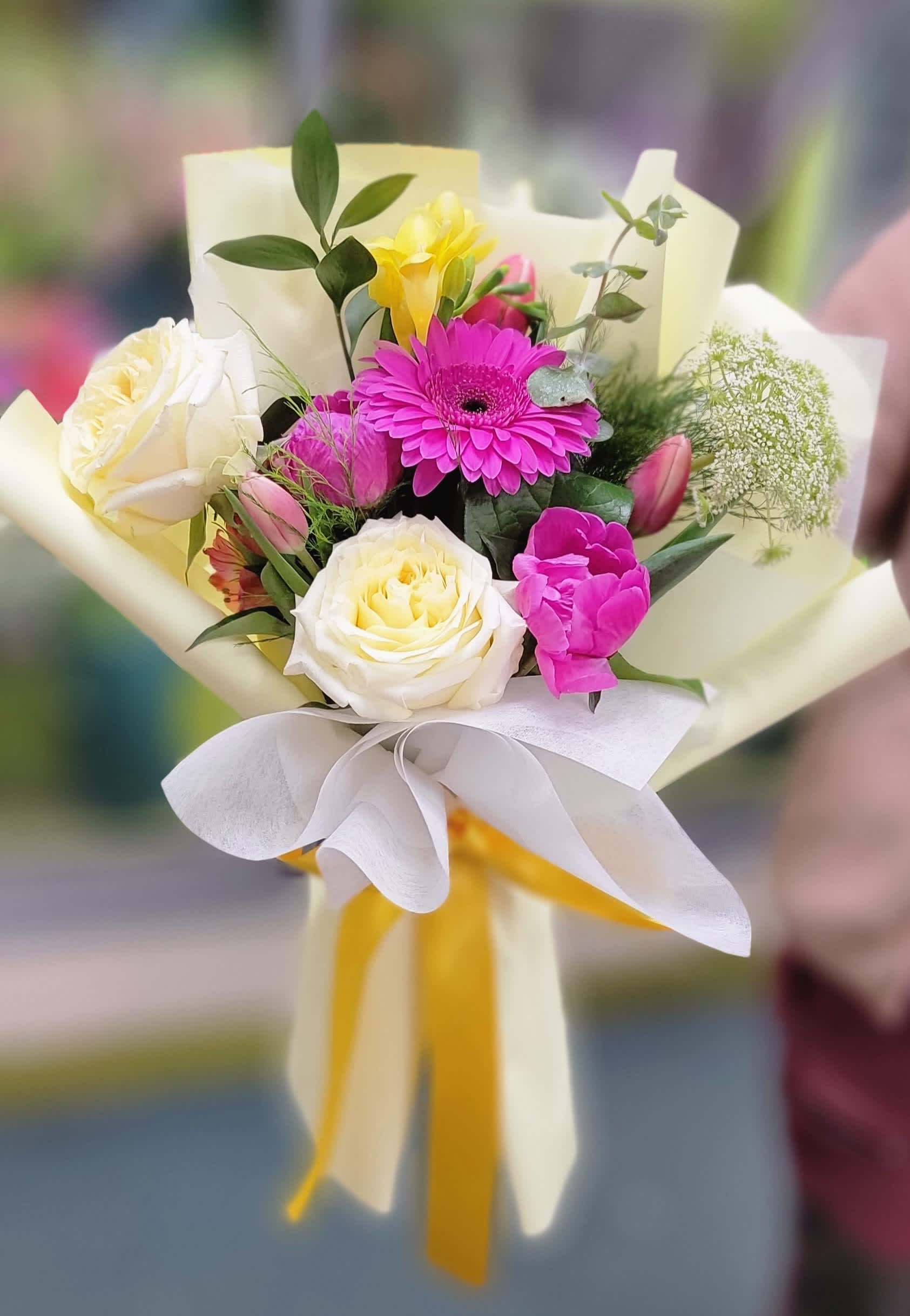 Bouquet of pink and white flowers wrapped in cream paper with a yellow ribbon